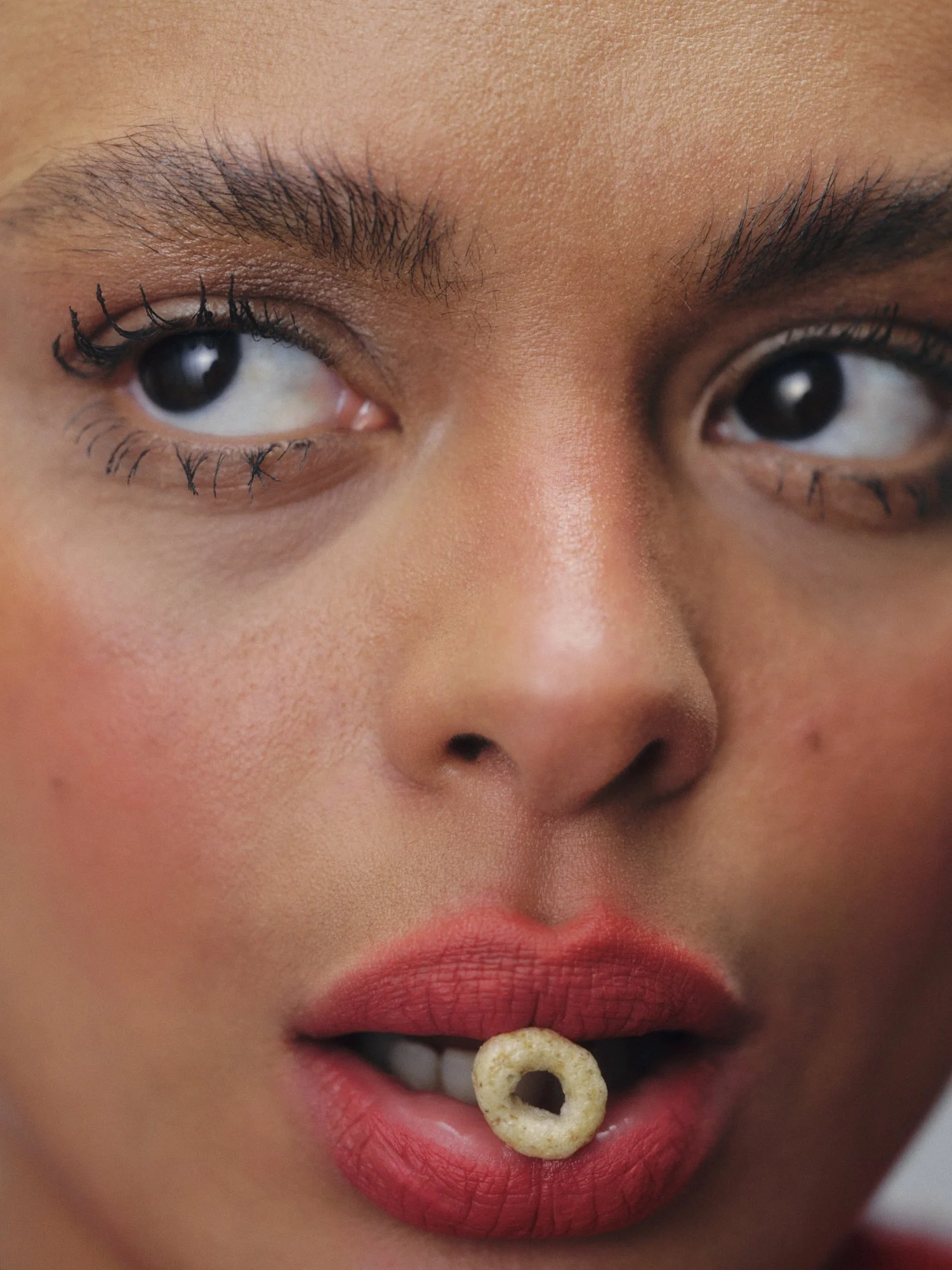 Close-up of a woman's face focusing on her eyes, lips, and a cereal ring held between her lips.