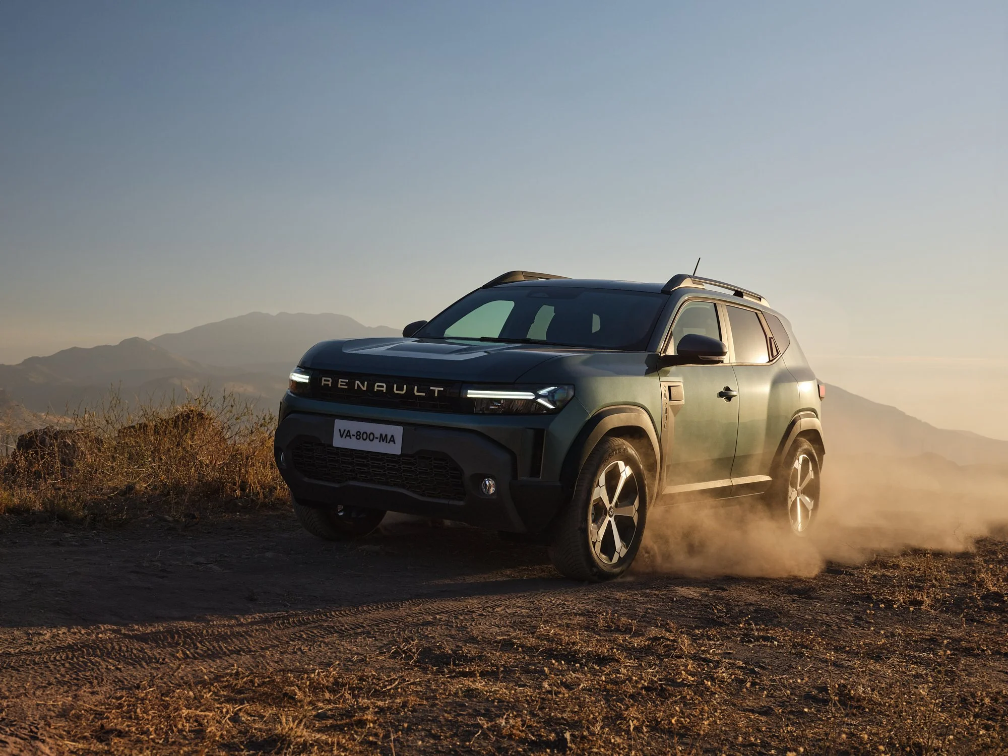 A black Renault SUV driving off-road on a dusty dirt trail in a mountainous landscape during sunset.