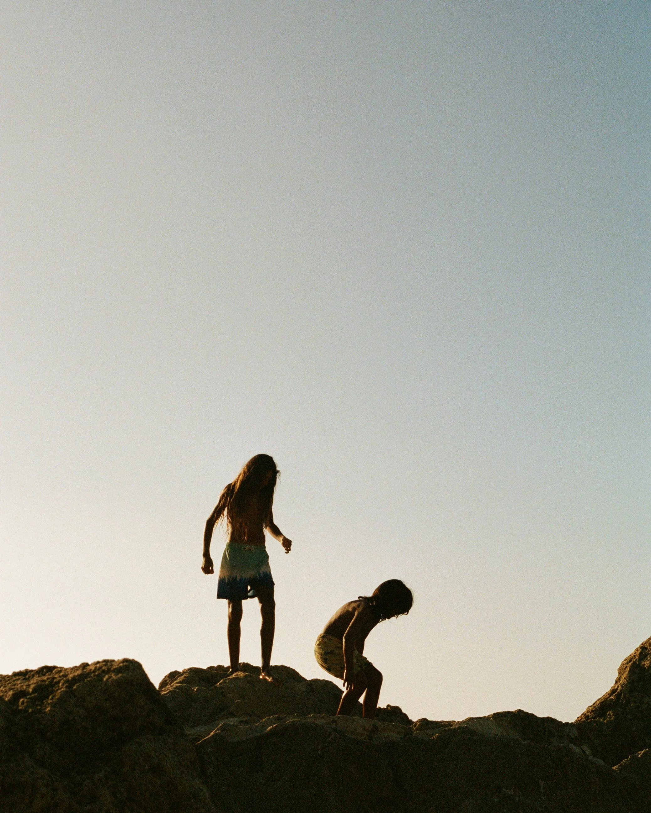 Two children playing on rocks at sunset, silhouette captured against the sky.