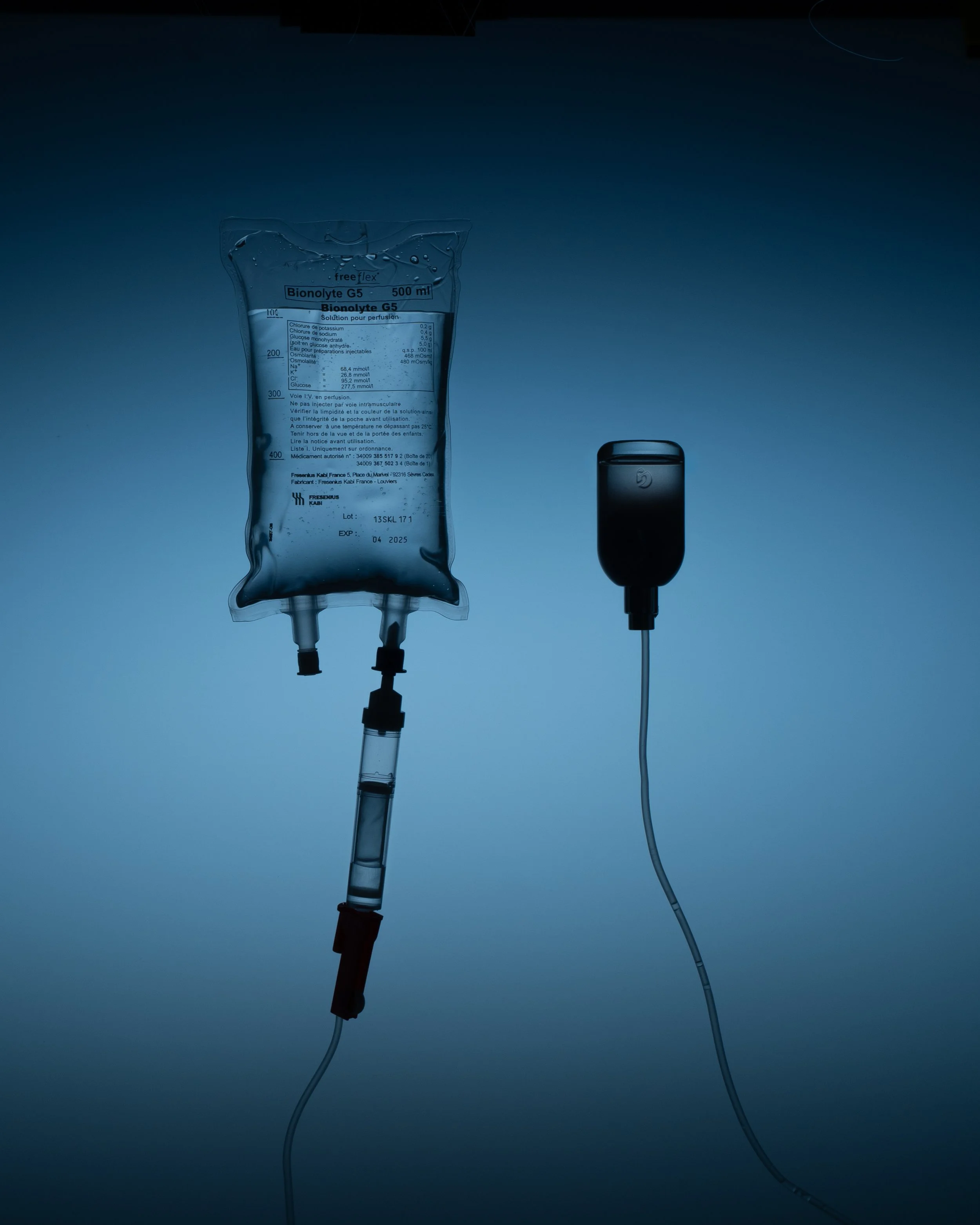 A medical IV bag labeled 'Bionolyte G5' connected to a syringe and an infusion pump with a power adapter, both positioned against a dark background.