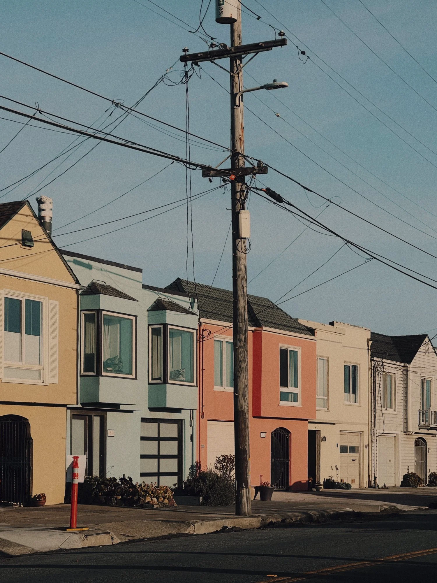 A row of colorful houses with front yards, a utility pole with electrical wires, and a clear blue sky.