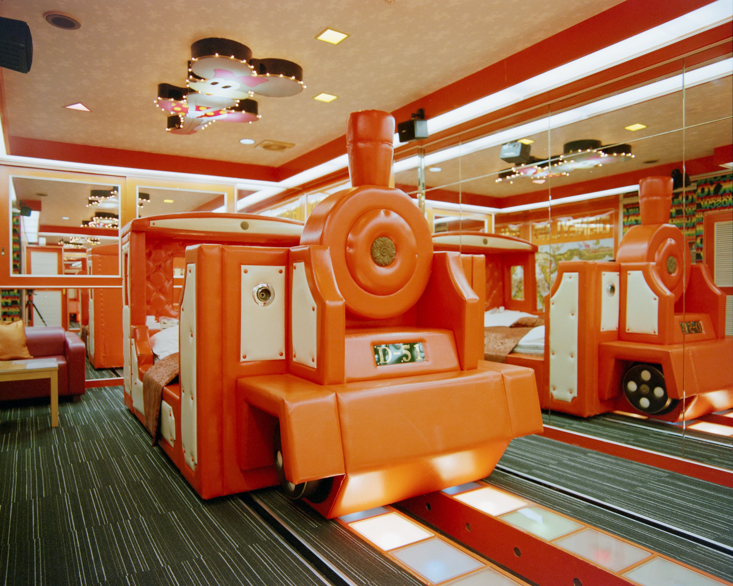 Indoor arcade with a large orange train-themed play structure and beds inside, mirrored walls, and colorful decor.