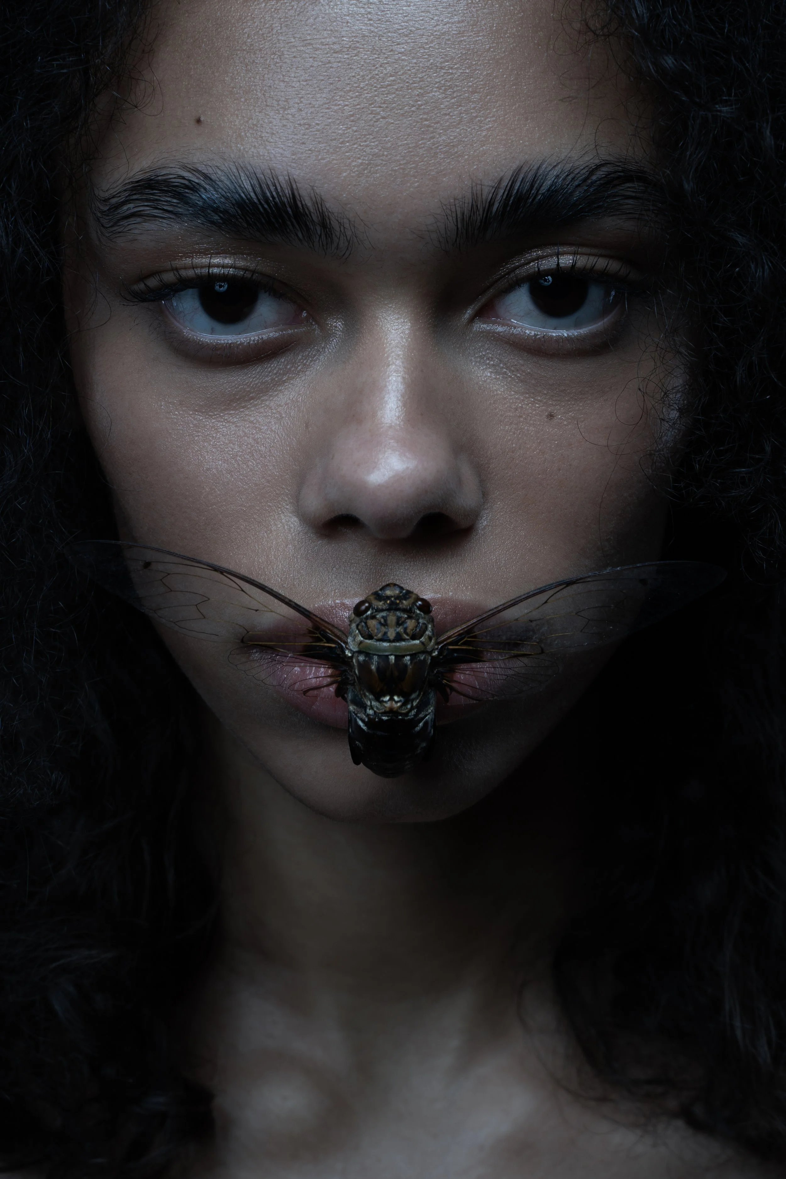 Close-up of a woman's face with a dragonfly resting on her lips.