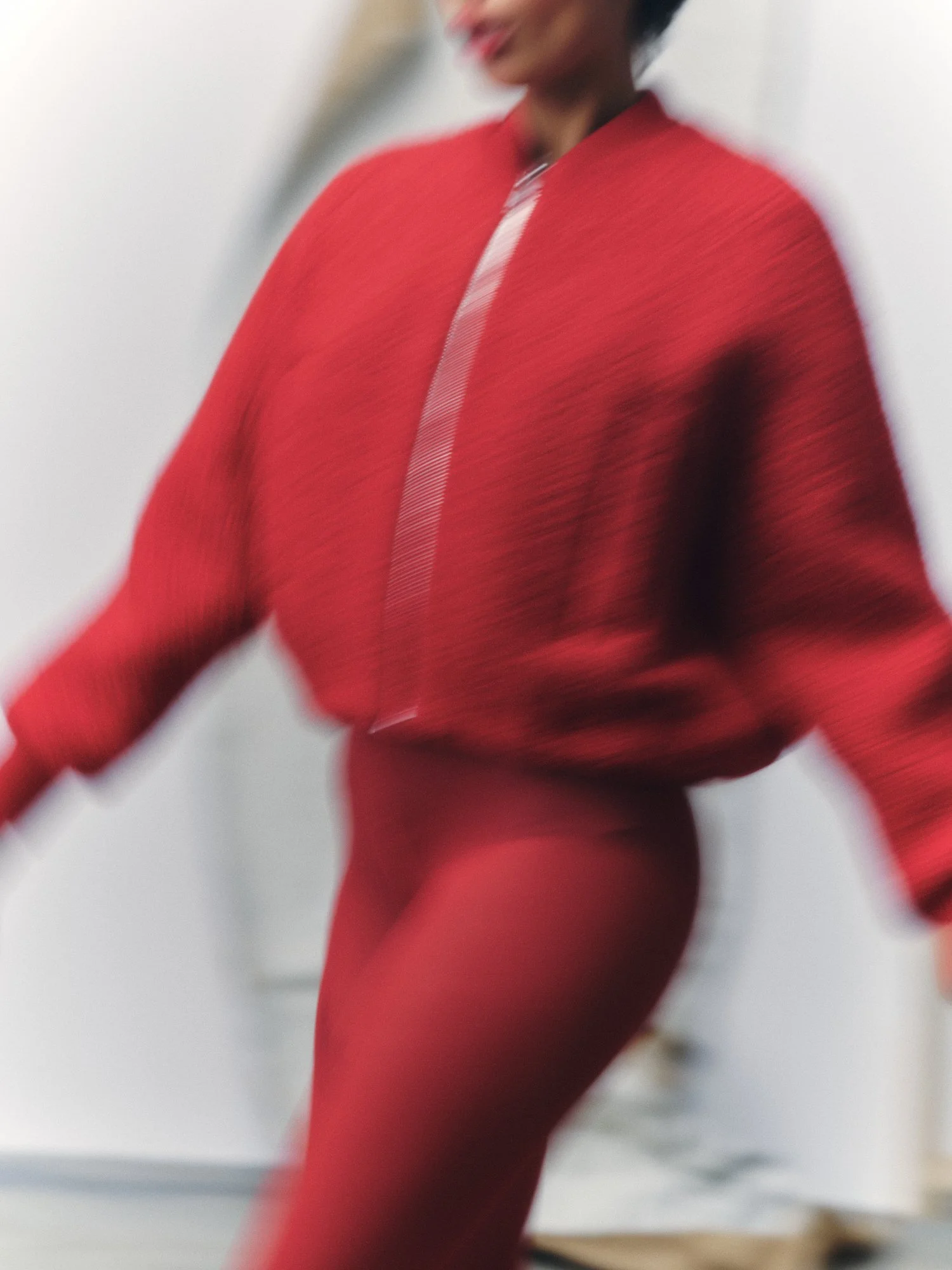 A person in a vibrant red outfit, possibly a dress or suit, photographed in motion with a blurred background, creating an artistic and dynamic composition.