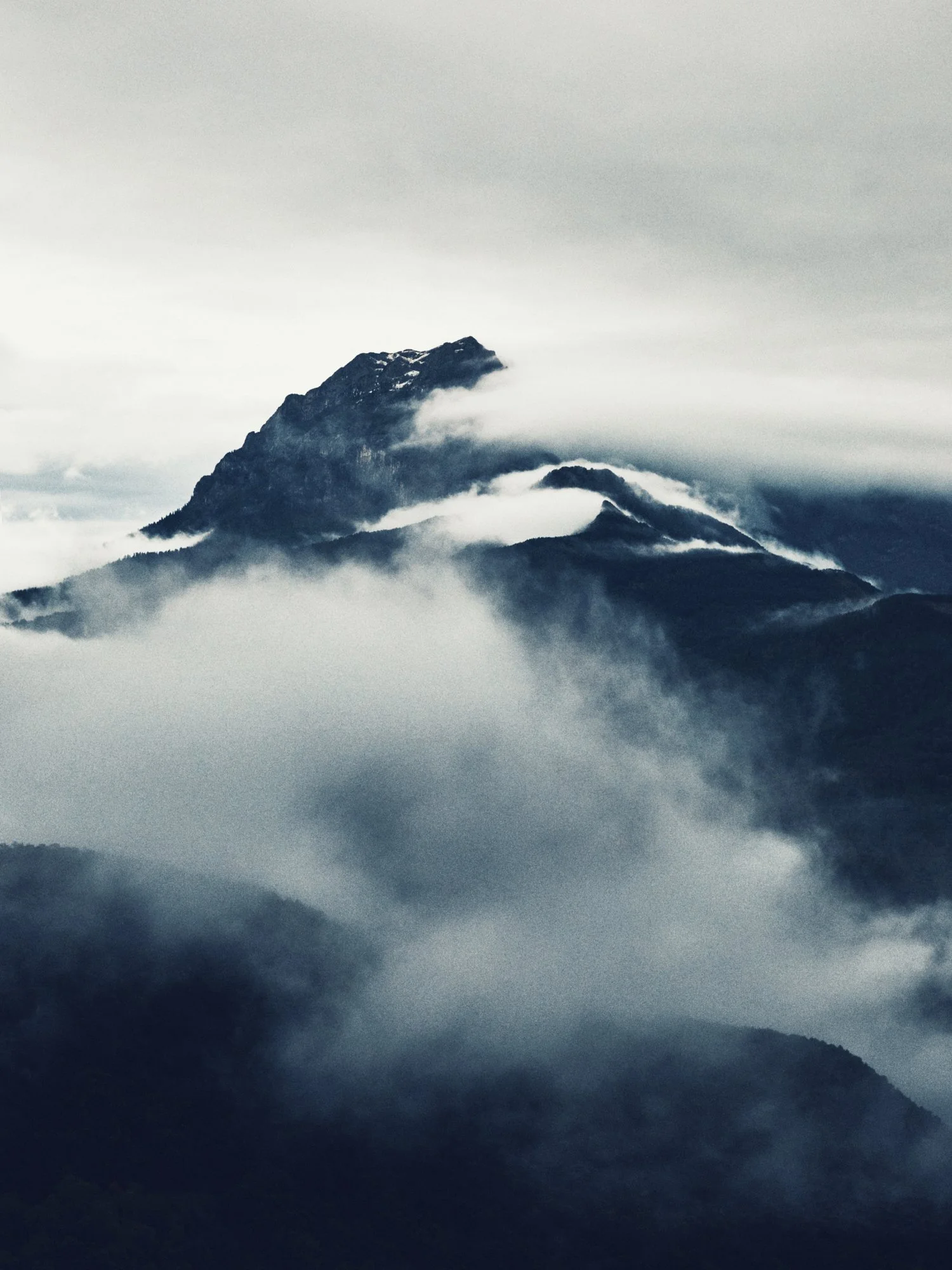 Mountains with snow and clouds surrounding the peaks, a misty and cloudy sky.