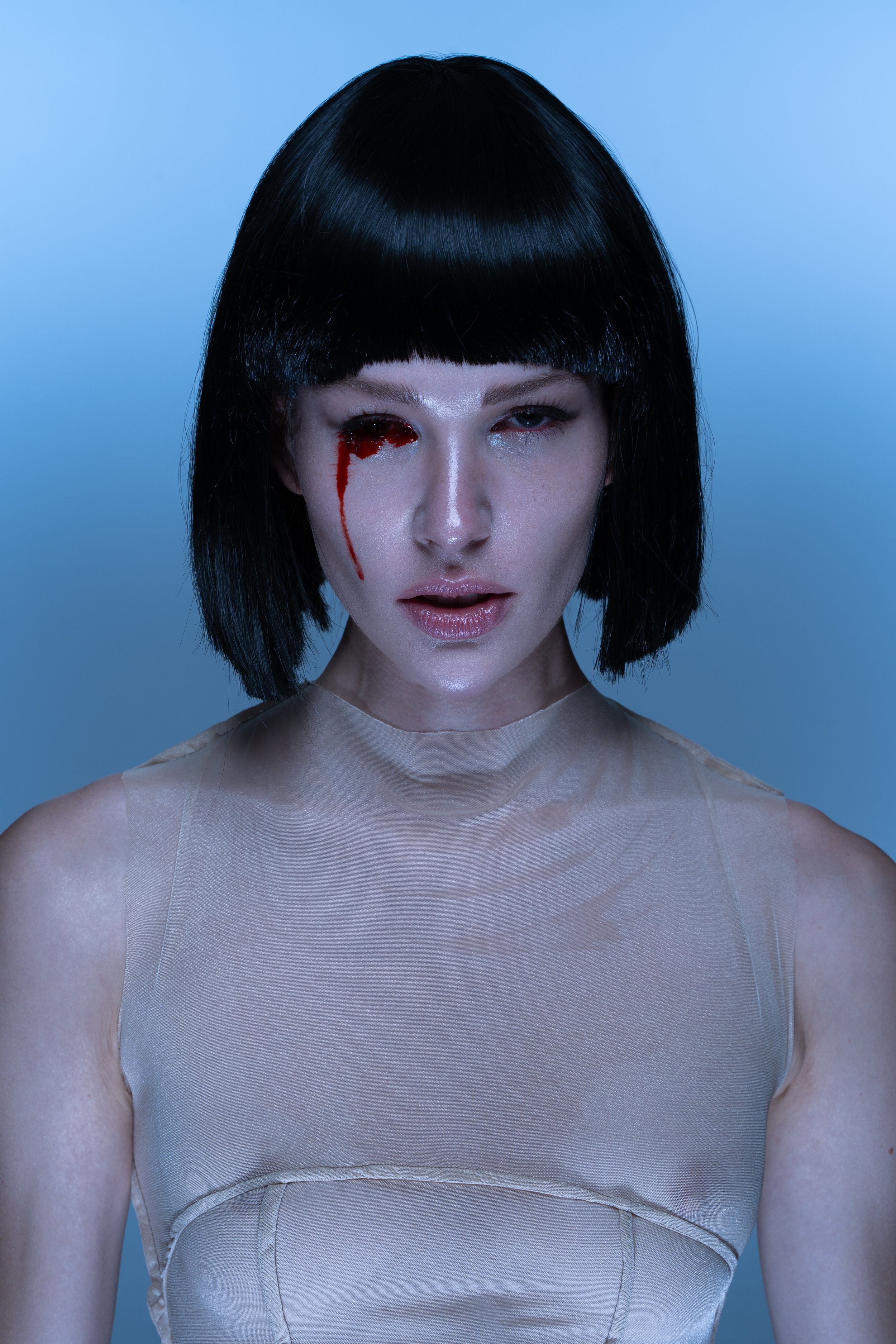 A woman with short black hair and a neutral expression, one eye appears injured with a blood-like effect. She wears a beige sleeveless top.