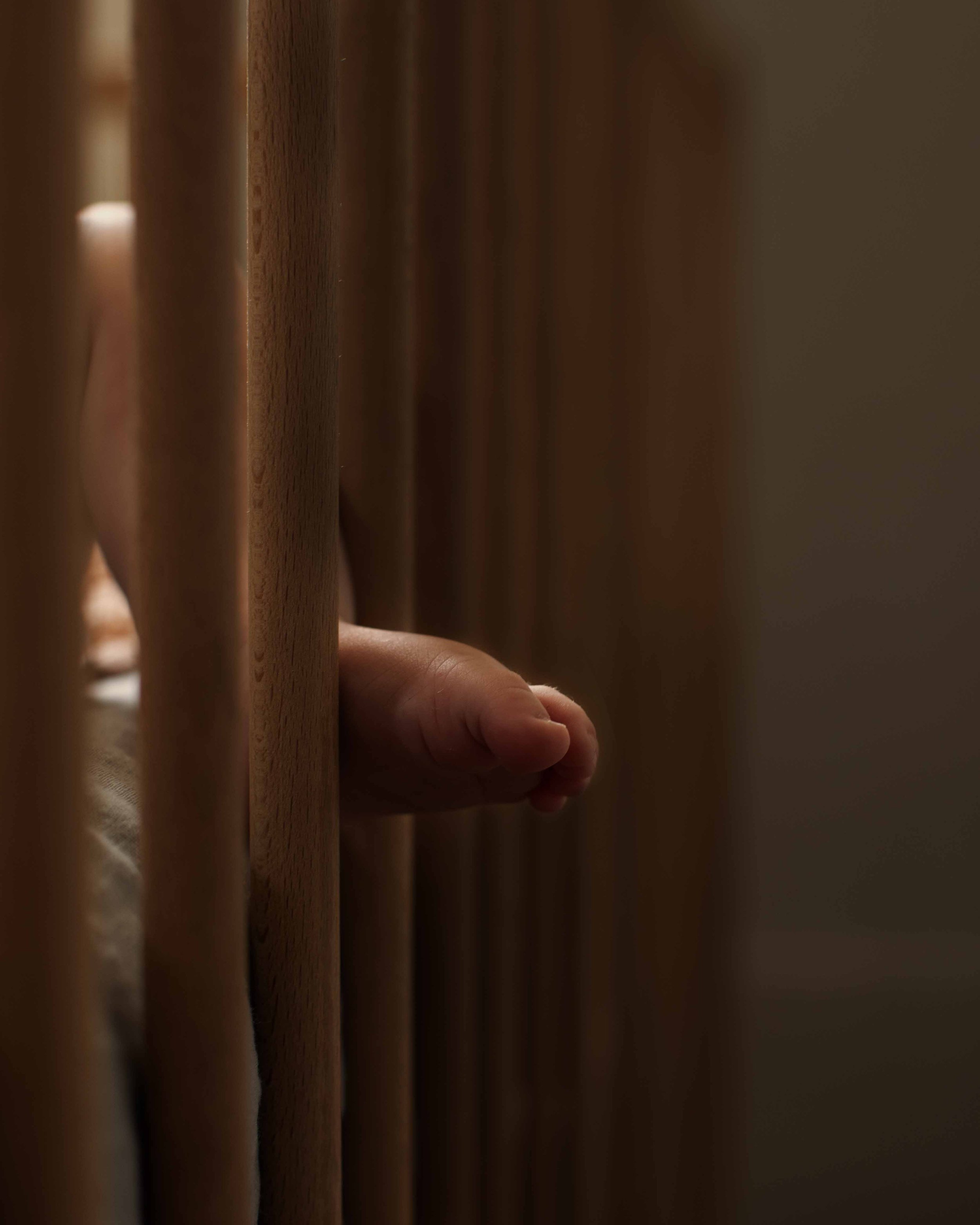 A baby's hand gripping a wooden crib rail.