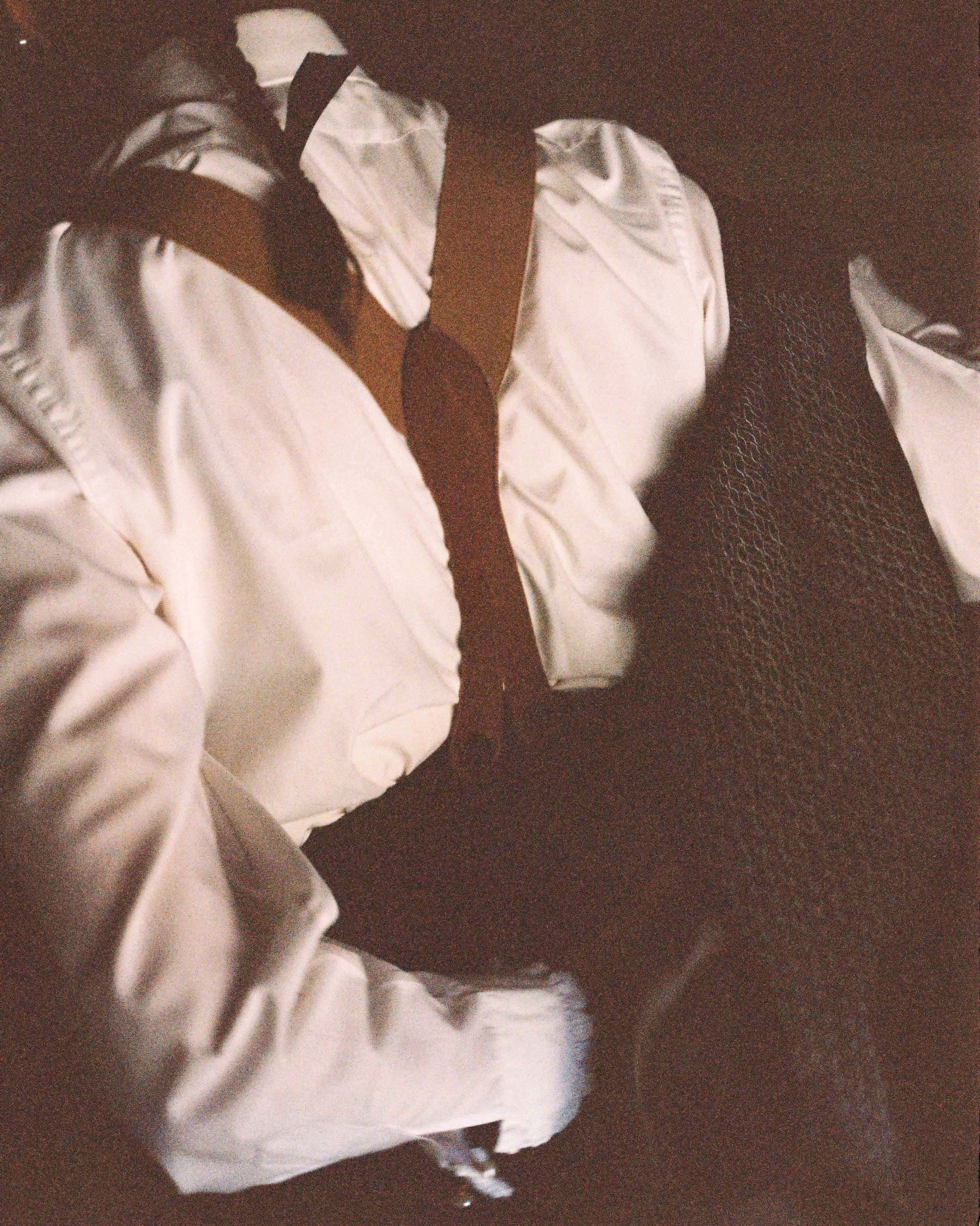 Close-up of a person wearing a white shirt, black tie, and black textured pants, laying down or resting on a surface.