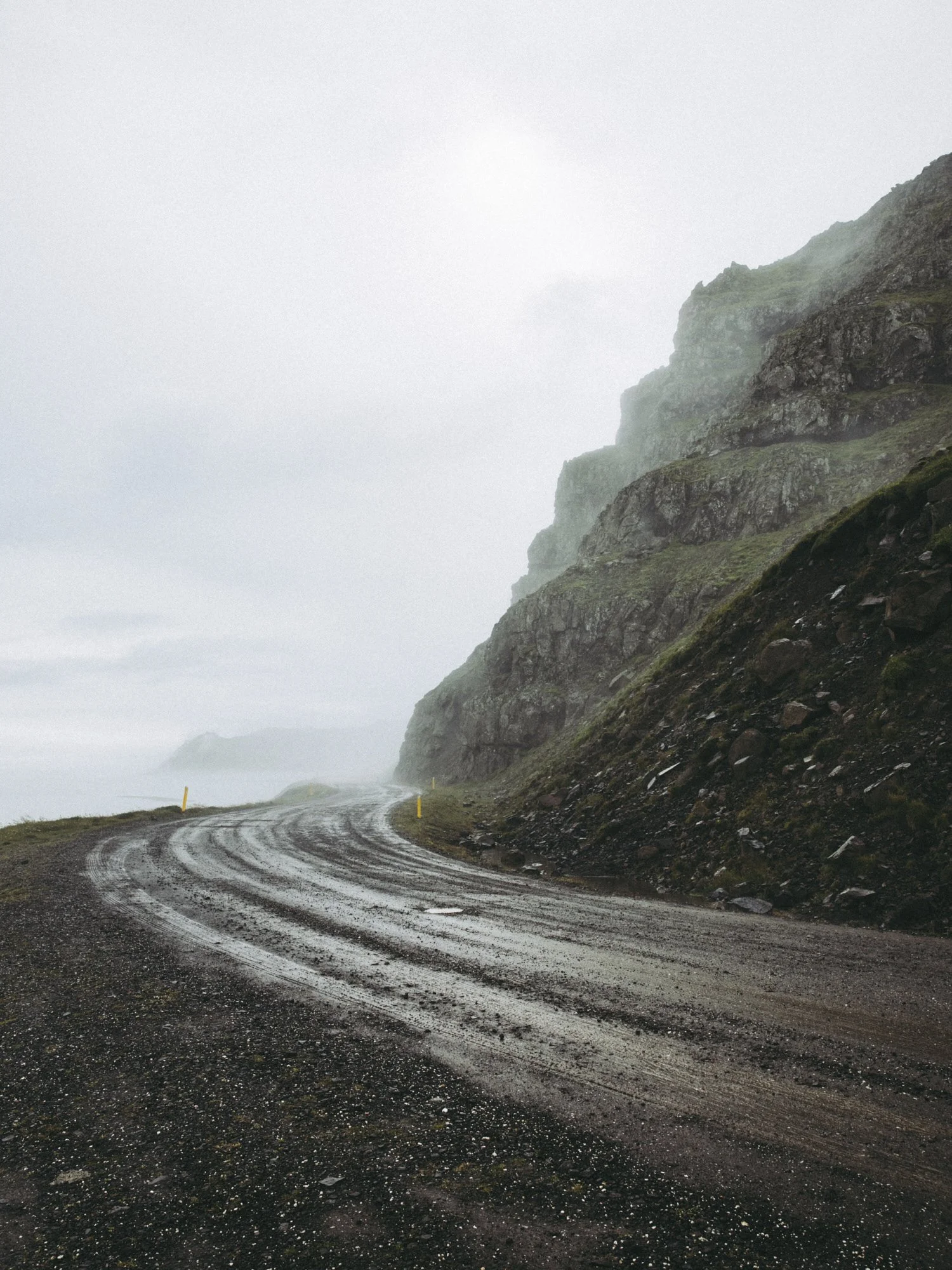 A winding gravel road next to rocky, green cliffs on a foggy day.