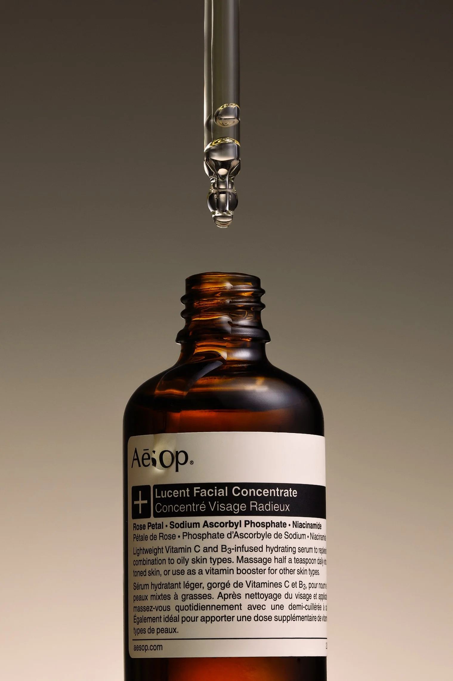 A brown glass bottle of Aesop Lucent Facial Concentrate with a dropper above, containing a few drops of serum.