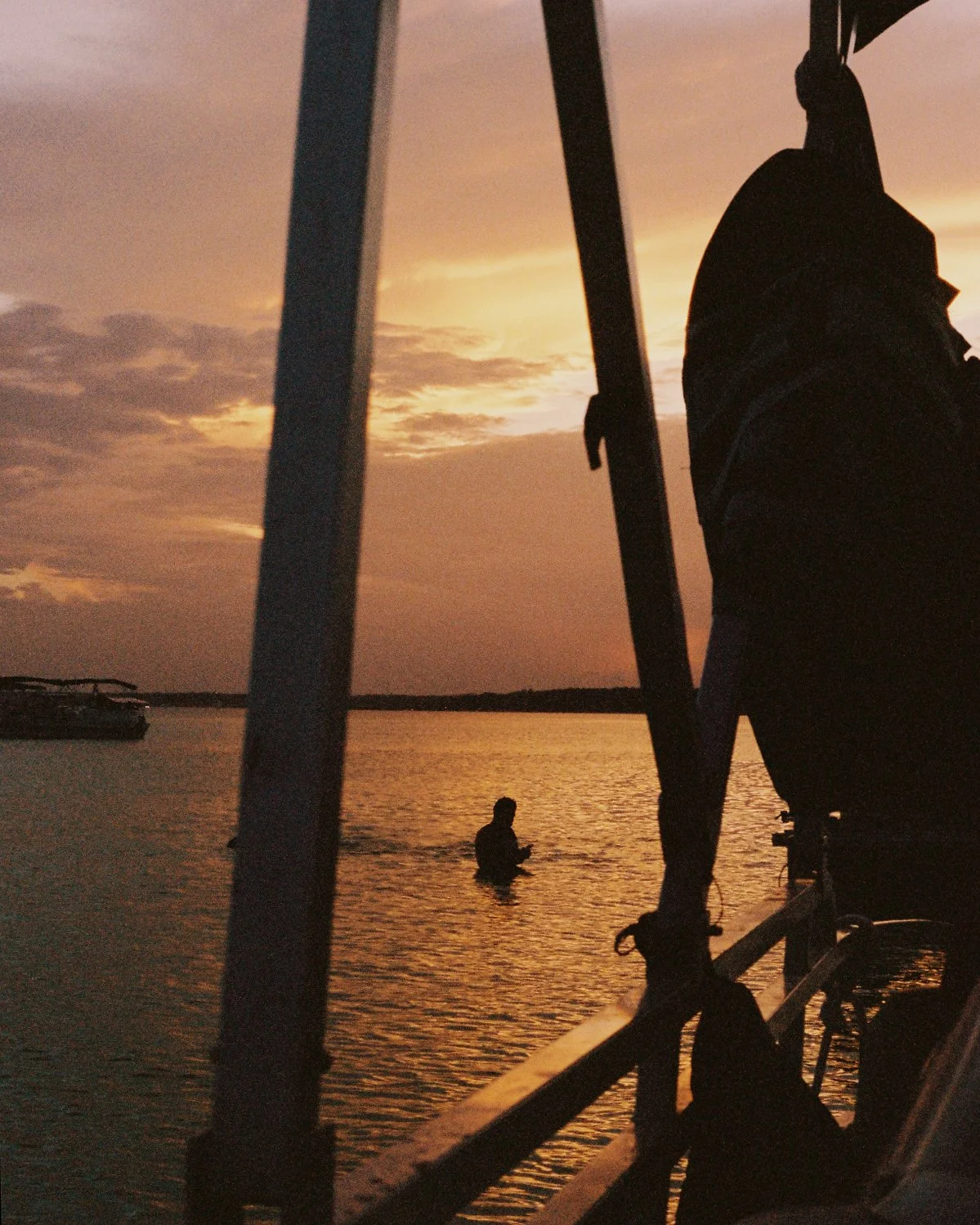 Silhouette of a person standing in water at sunset, viewed from a boat with part of the boat and a bicycle in the foreground.