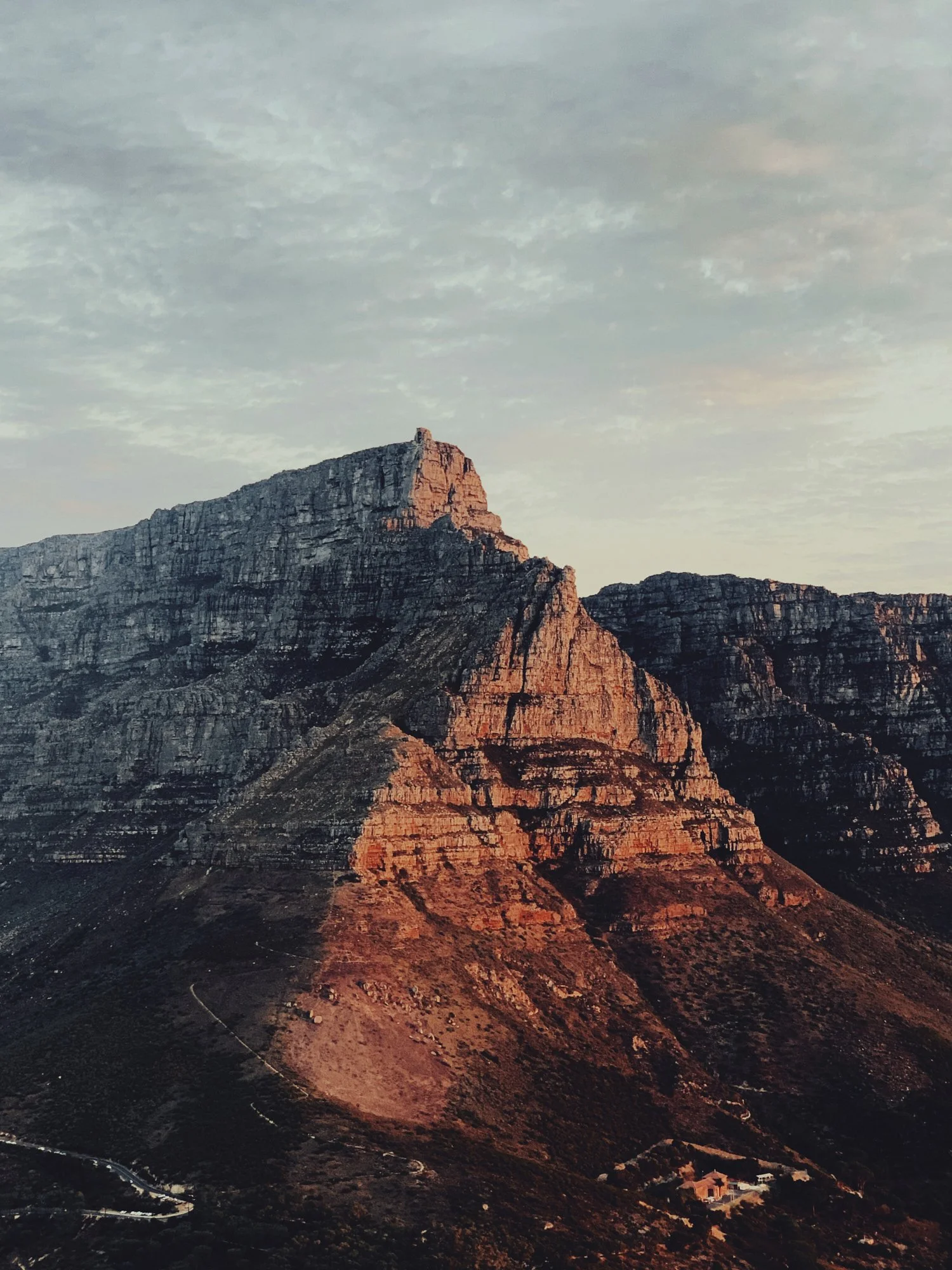Sunset illuminating the rugged cliffs of a mountain range with exposed layers of rock and sparse vegetation at the base.