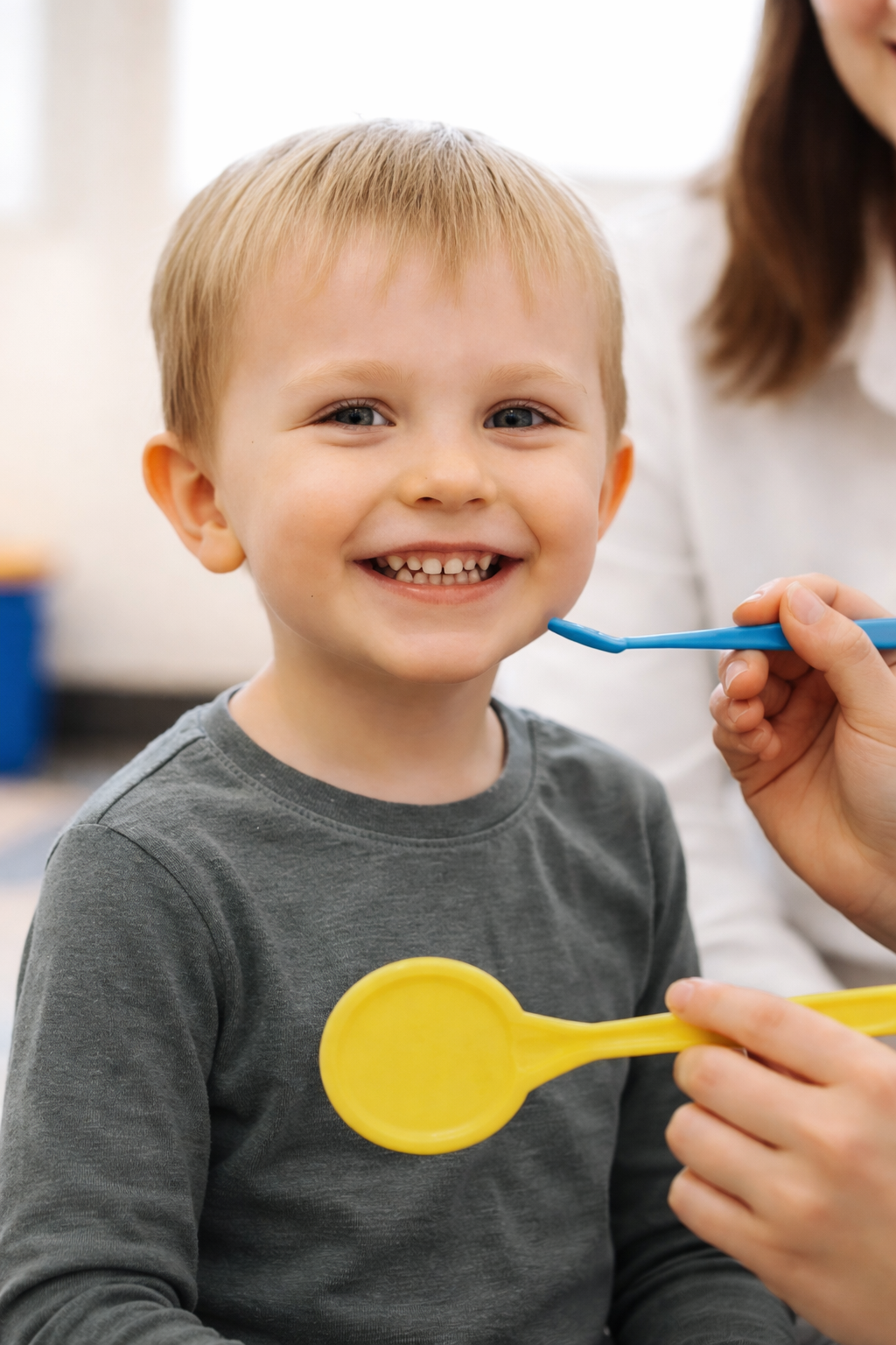 Young boy smiling while being examined with a tongue depressor by a healthcare professional.