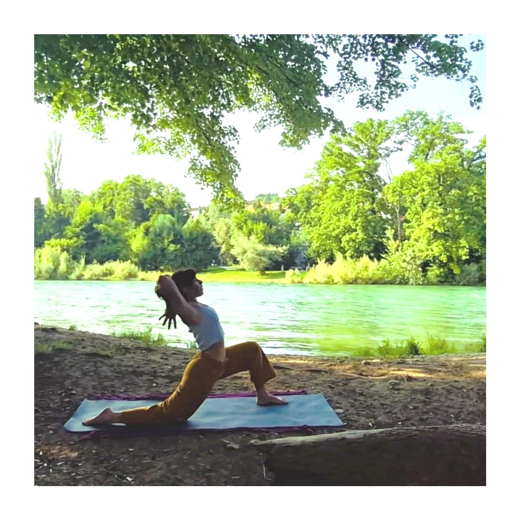Person practicing yoga on a mat by a river, surrounded by lush green trees in a park.