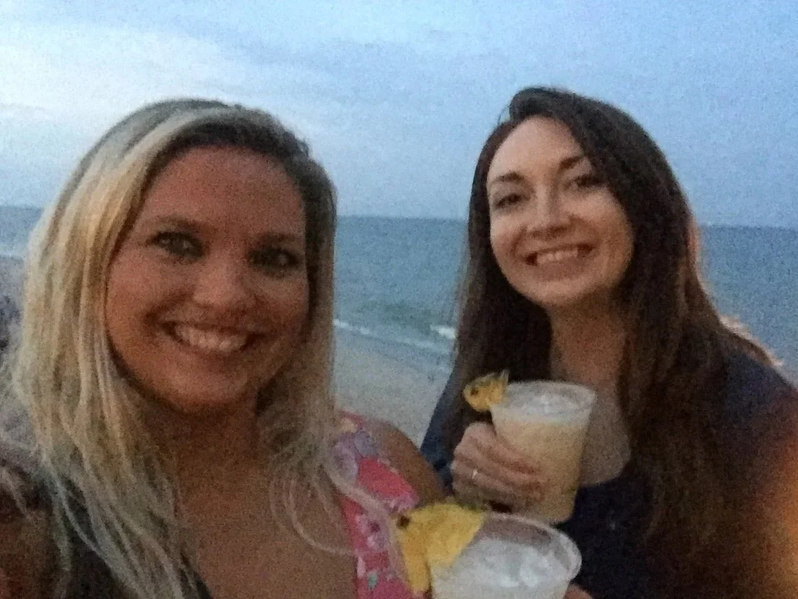 My cousin and I smiling at Carolina Beach at sunset, holding our first beach vacation pina coladas.