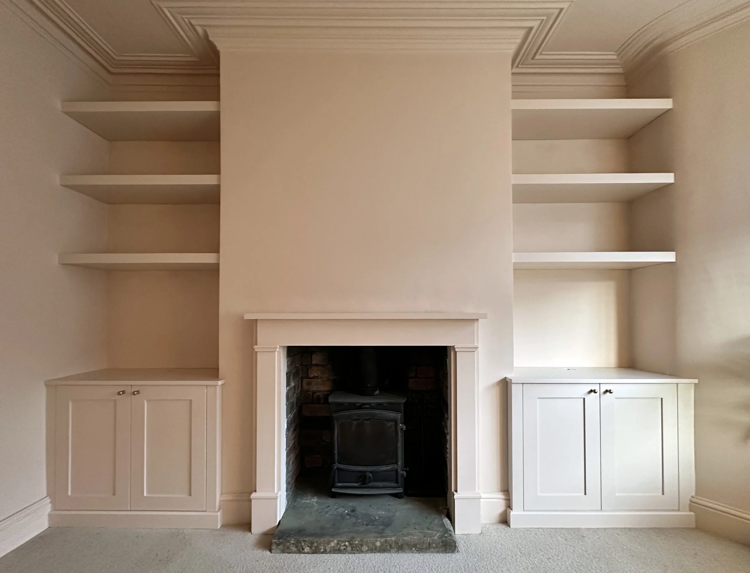 Bespoke fitted alcove cabinets for TV and hi-fi. Spray finished in flat F&B Pink Ground with oak interiors. Clever cable management, Blum hardware, floating shelves above.