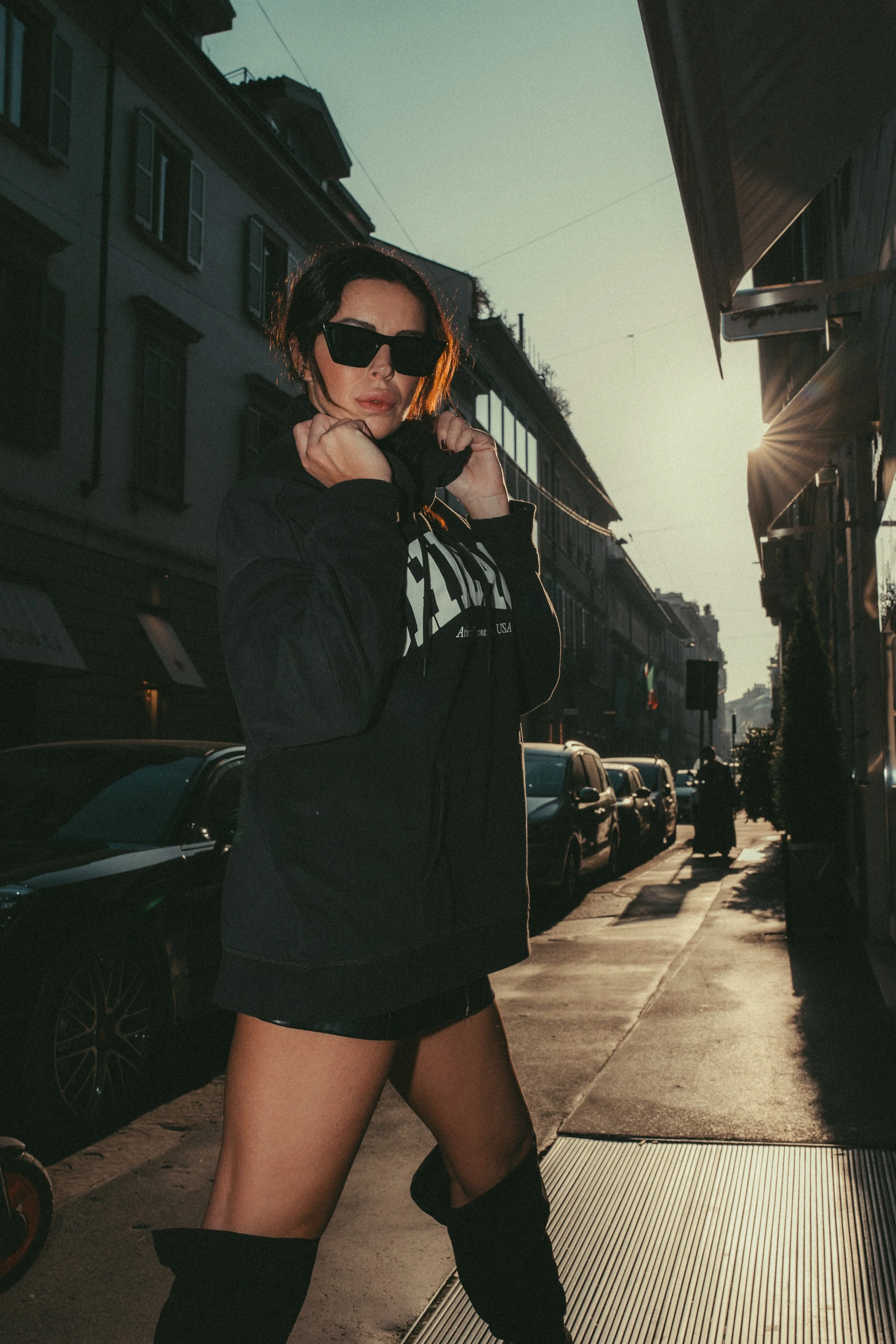 Fashion portrait woman black jacket skirt thigh-high boots Milan sidewalk sunset — Nicco Mandelli