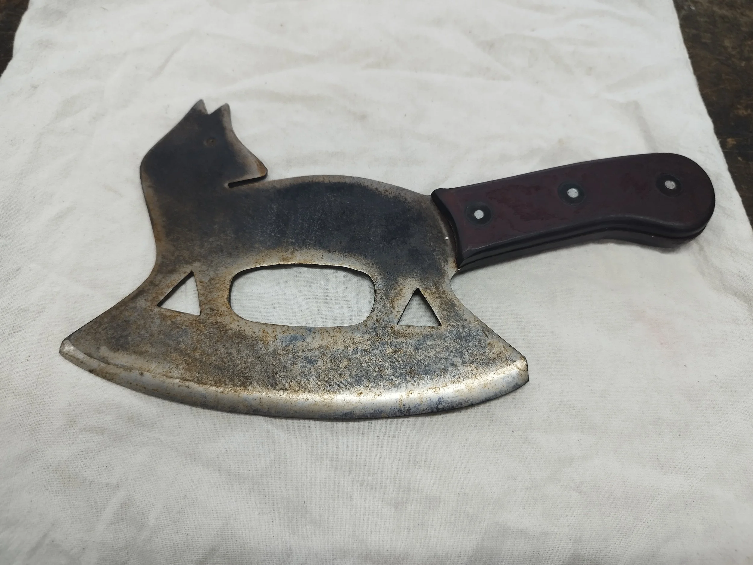 Ein selbstgebautes Messer in Form eines Katzenkopfes mit einem schwarzen Griff liegt auf einem weißen Tuch.