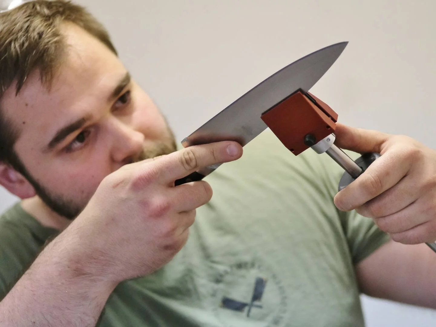 Ein junger Mann mit braunen Haaren und Bart arbeitet mit einem Handwerkzeug an einem kleinen Metallstück.