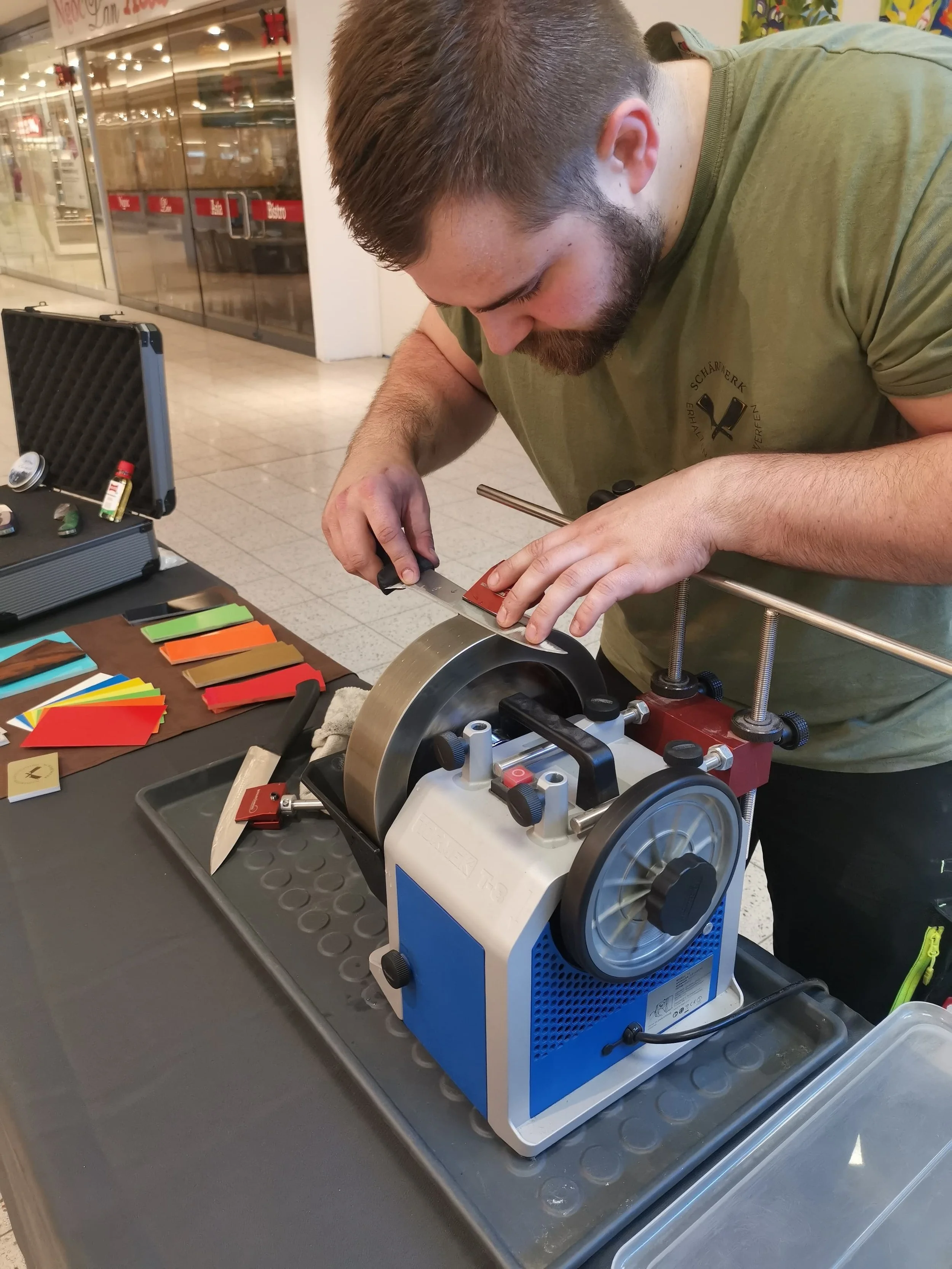 Ein Mann arbeitet mit einem Schmuckuhren-Poliergerät an einem Fototisch, auf dem bunte Leder- oder Gummibänder liegen.