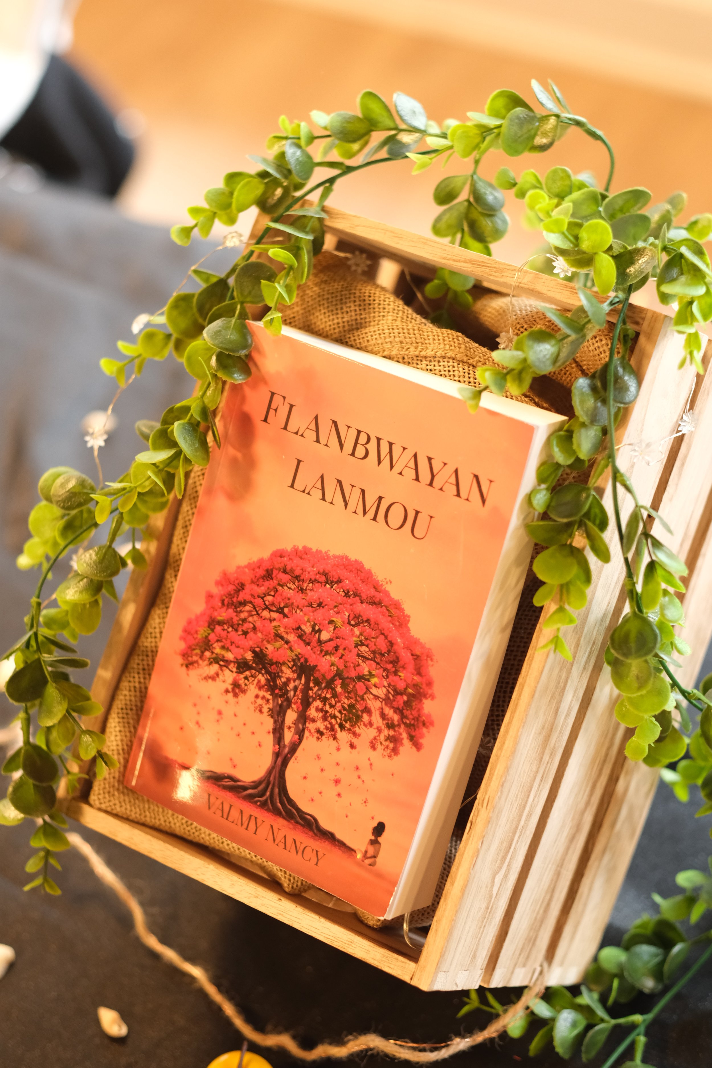 Un livre intitulé 'Flanbwayan Lamou' avec une illustration d'un arbre et une silhouette d'enfant, entouré de guirlandes de feuilles vertes.