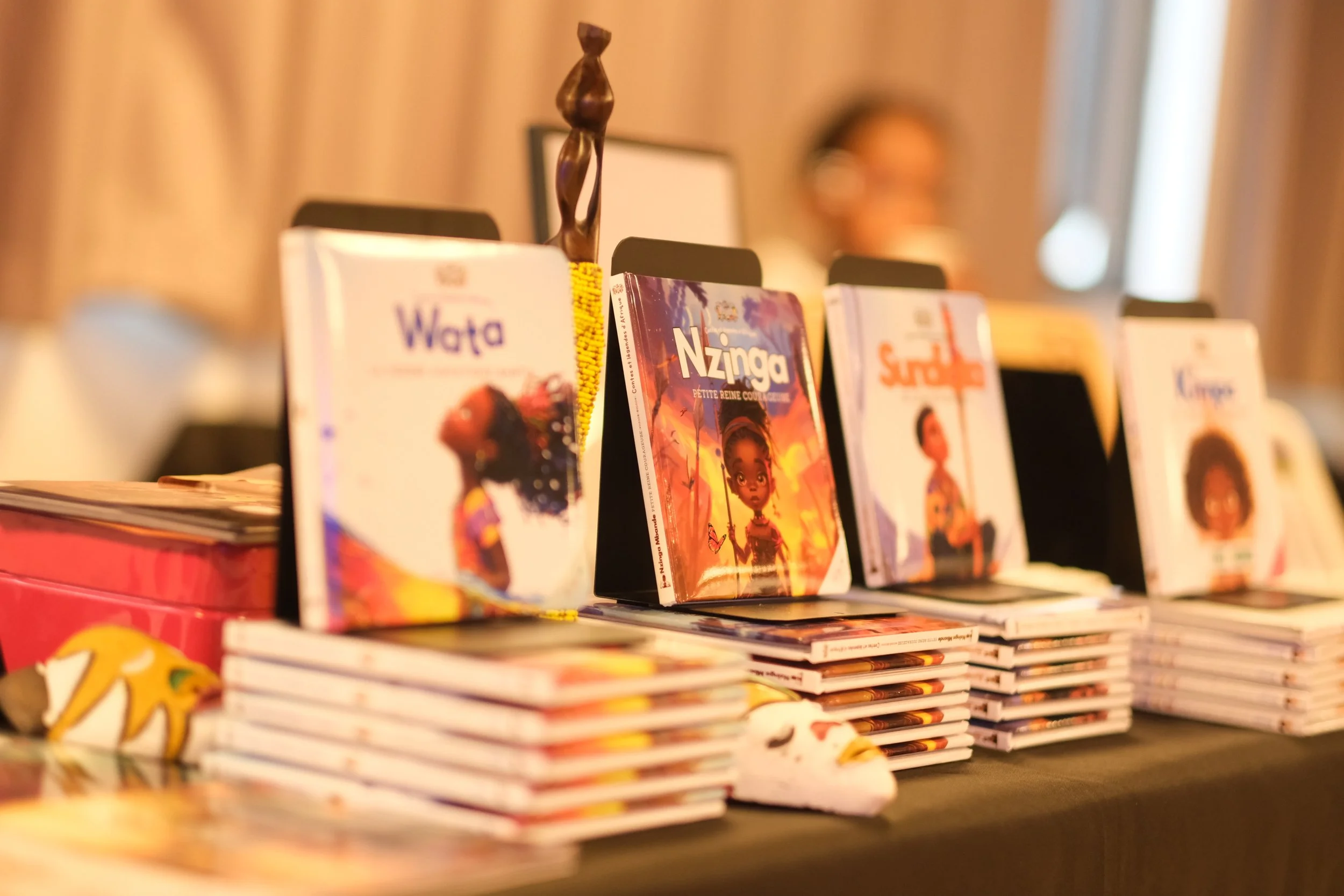 Livres pour enfants exposés sur une étagère, avec une poupée en bois en arrière-plan.