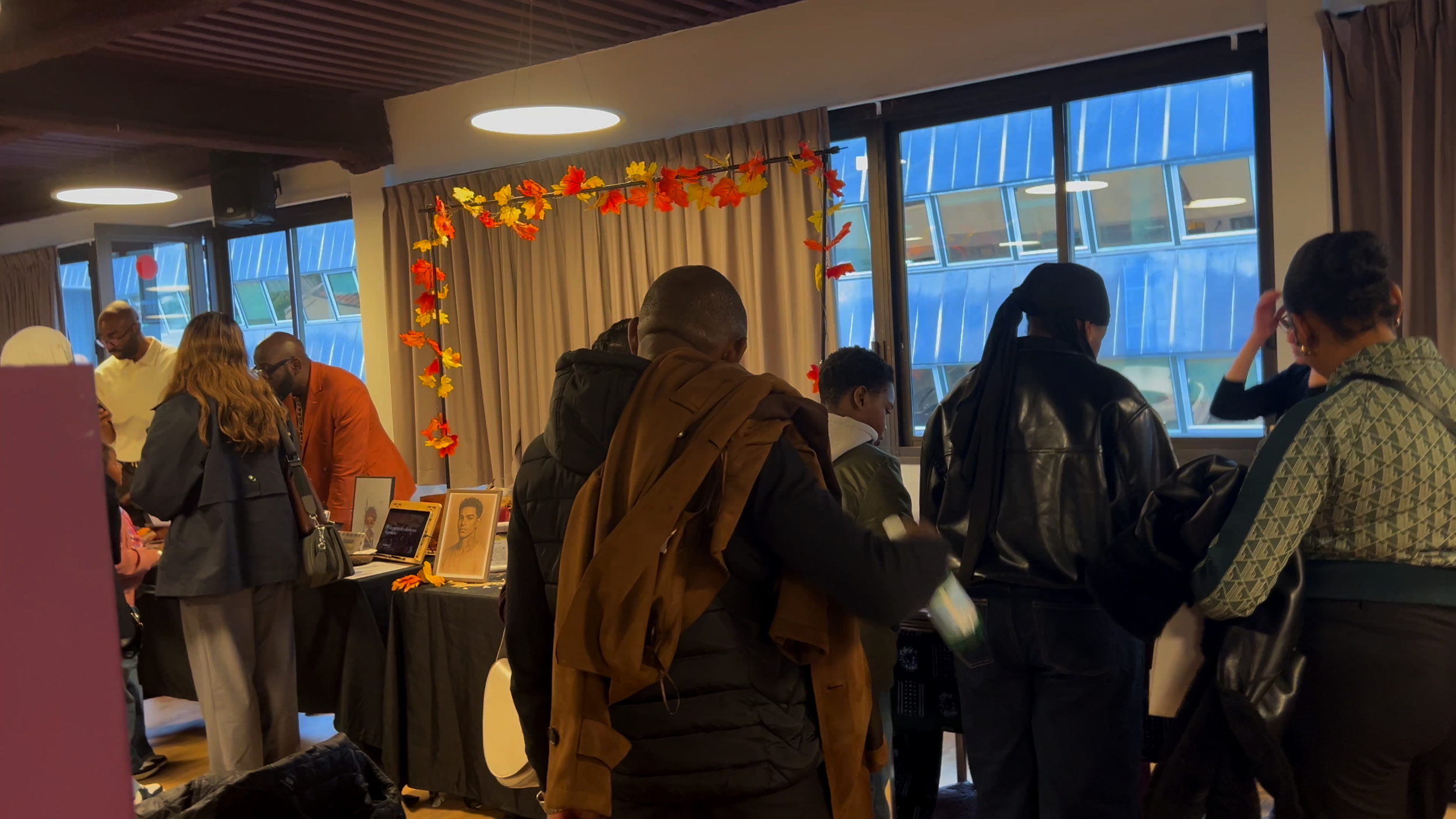 Groupe de personnes debout autour d'une table dans une pièce, décorations automnales avec feuilles en papier orange et jaune, affiches de personnalités sur la table.