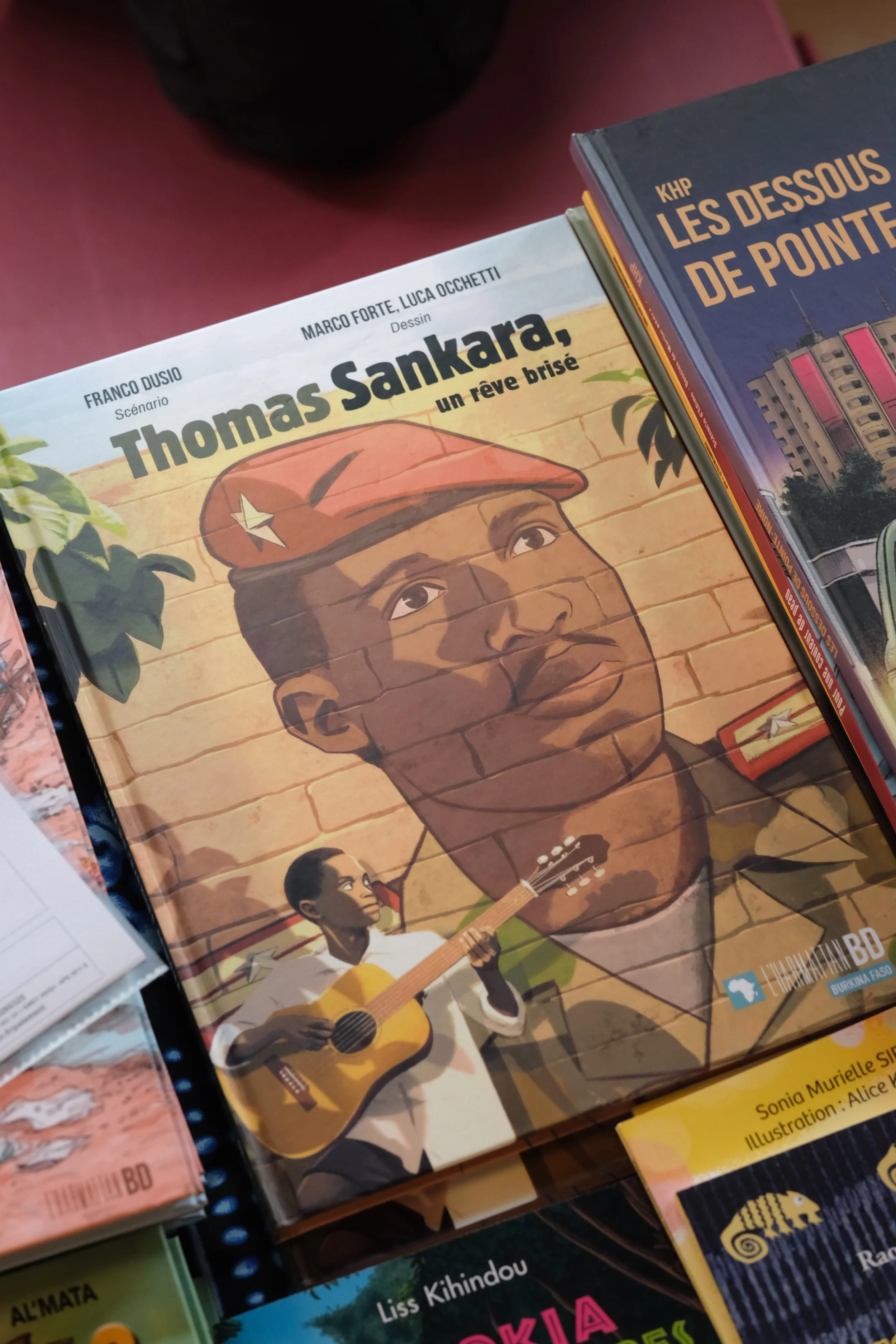 Livre avec une illustration d'un homme portant un béret rouge et jouant de la guitare, un autre enfant joue aussi de la guitare, sur la couverture d'un livre intitulé "Thomas Sankara, un rêve brisé".