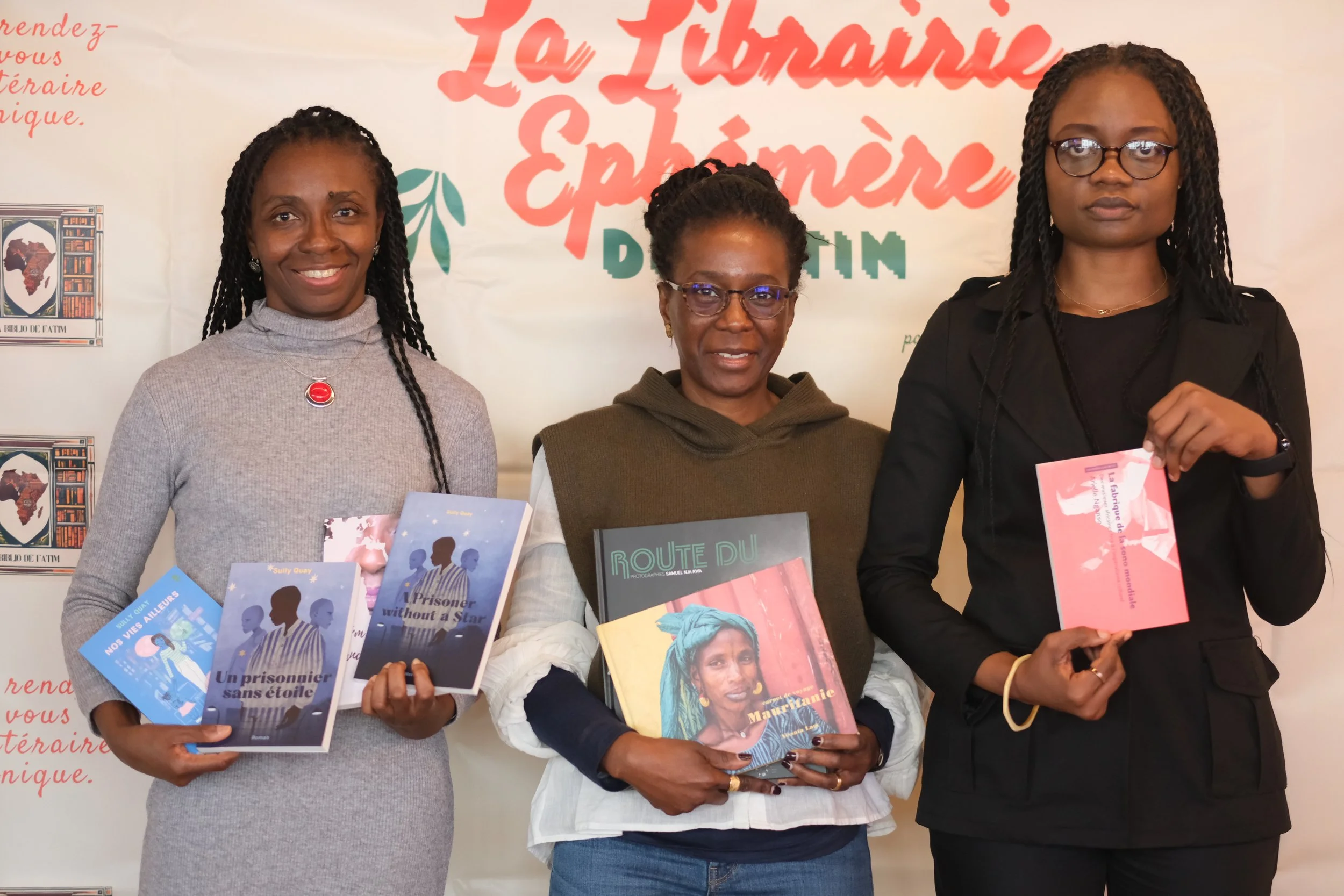 Trois femmes debout tenant des livres devant un panneau avec du texte en français. Elles posent pour une photo lors d'un événement littéraire ou culturel.