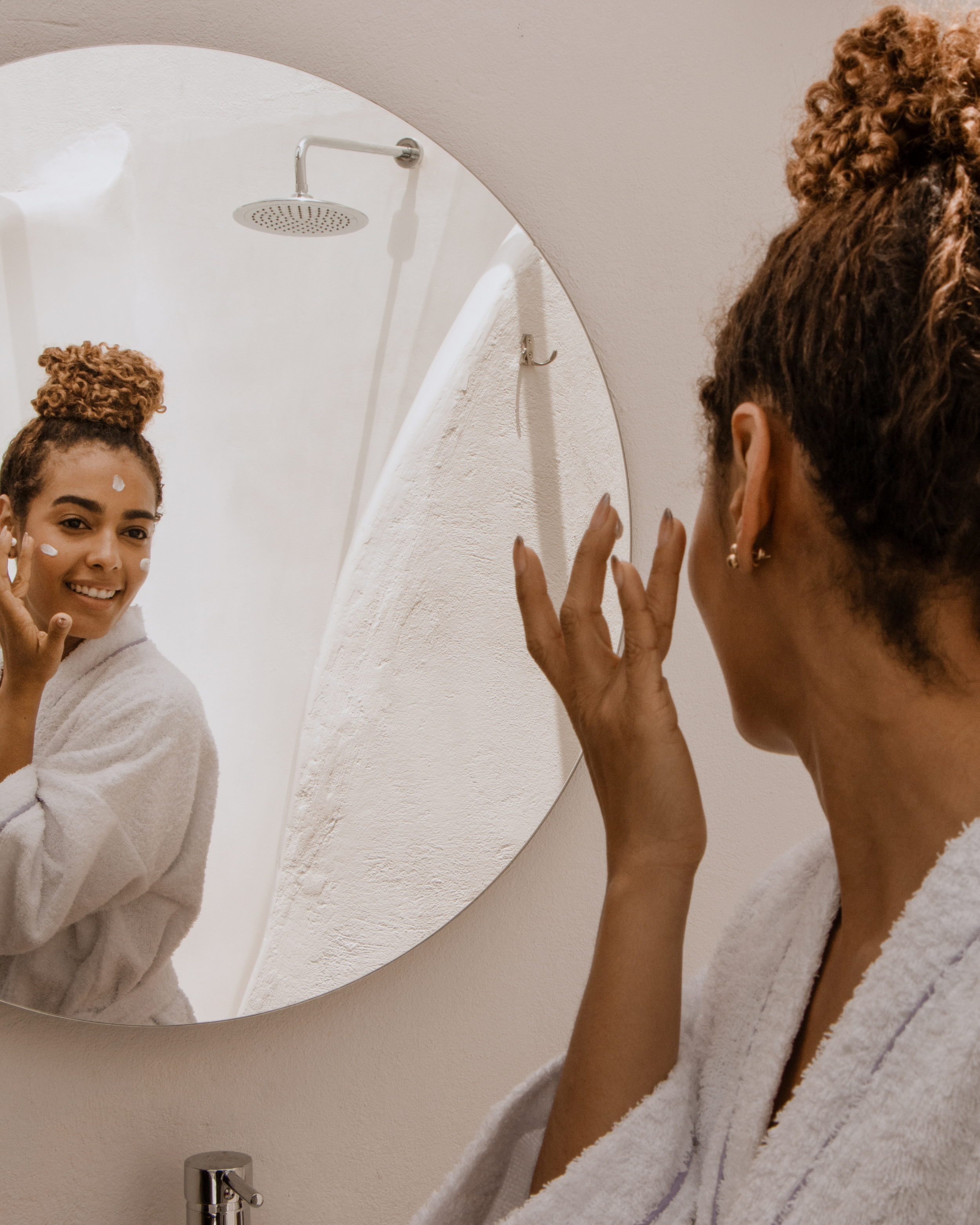Woman smiling at her reflection in the mirror applying cream to her face