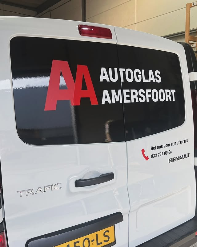 Rear view of a white Renault Trafic van with advertising for Autoglas Amersfoort, a glass repair business, on the back window and side door.