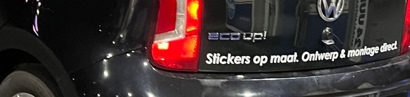 Close-up of the back of a black Volkswagen car with stickers and decals, including a sticker with the text 'Stickers op maat. Ontwerp & montage direct' and a Volkswagen logo.