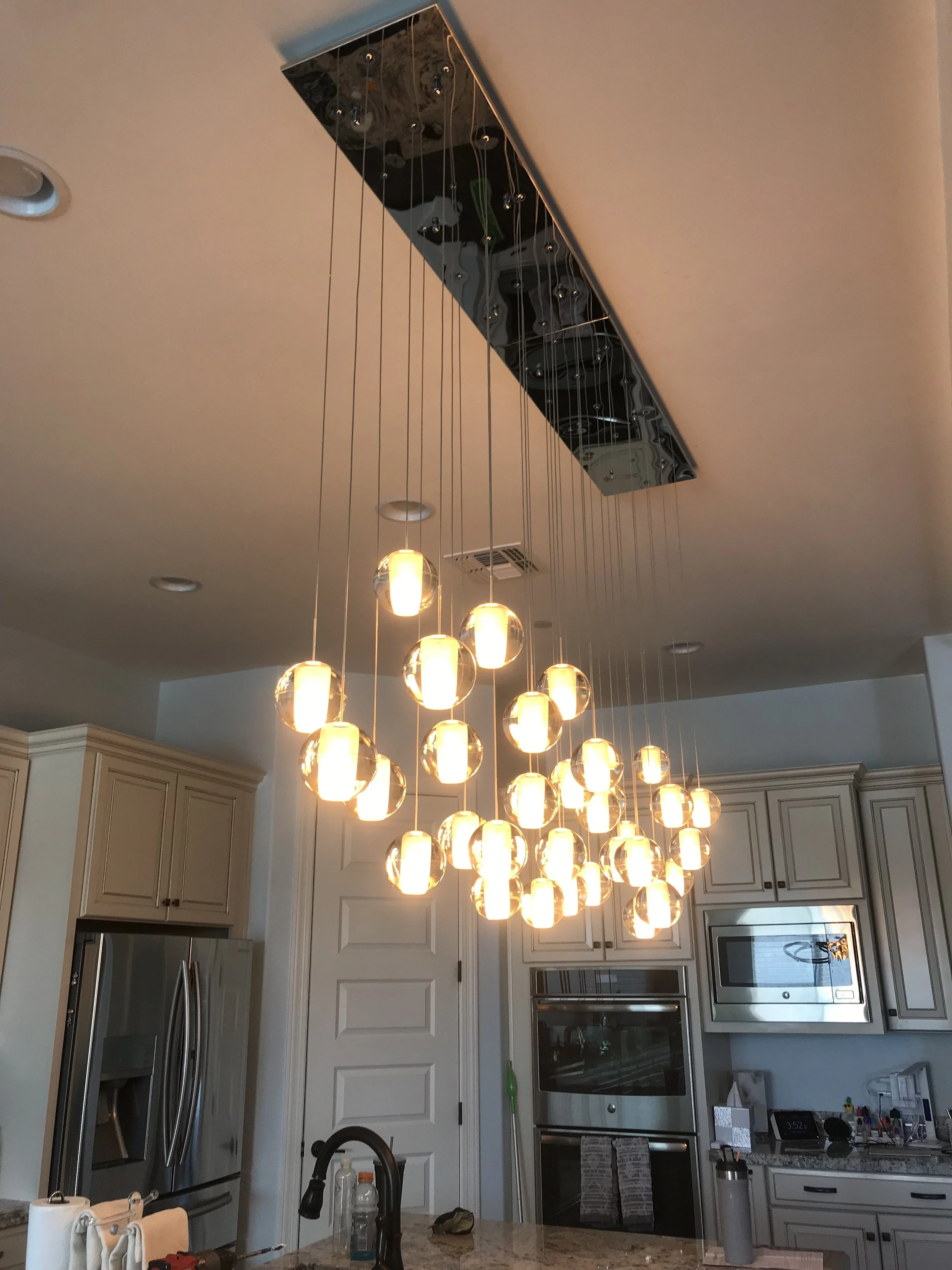 Modern kitchen with a cluster of pendant lights hanging from a reflective ceiling panel. Electrical Services | Rio Rancho, NM |
