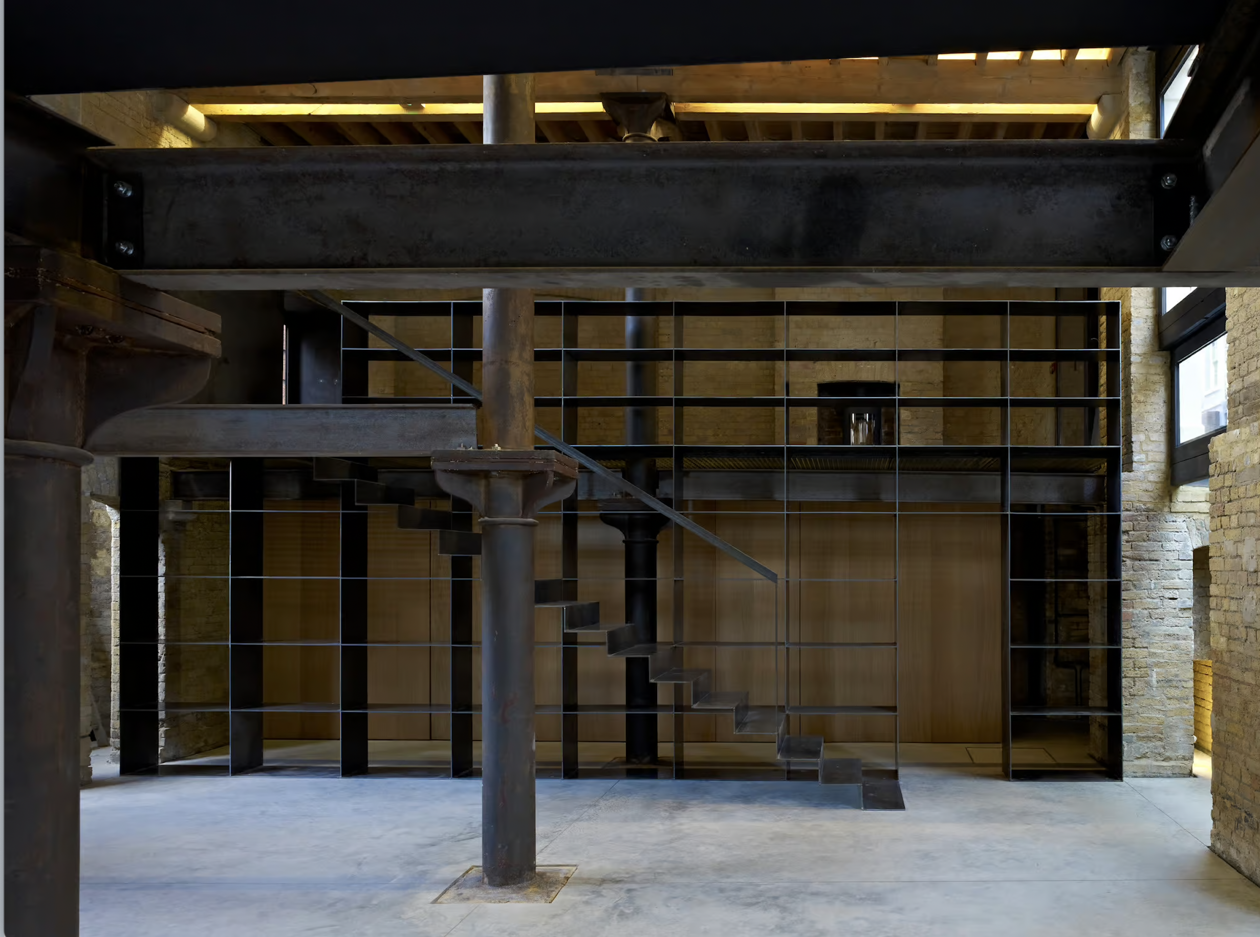 Interior view of a modern industrial-style space with metal staircase, black metal shelving, and exposed brick walls.
