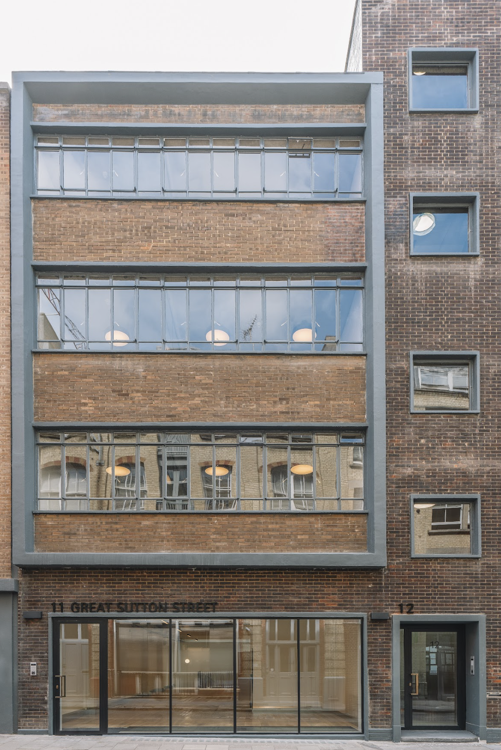 Modern brick building with large glass windows and small upper windows, with the address 11 Great Sutton Street visible above the entrance.