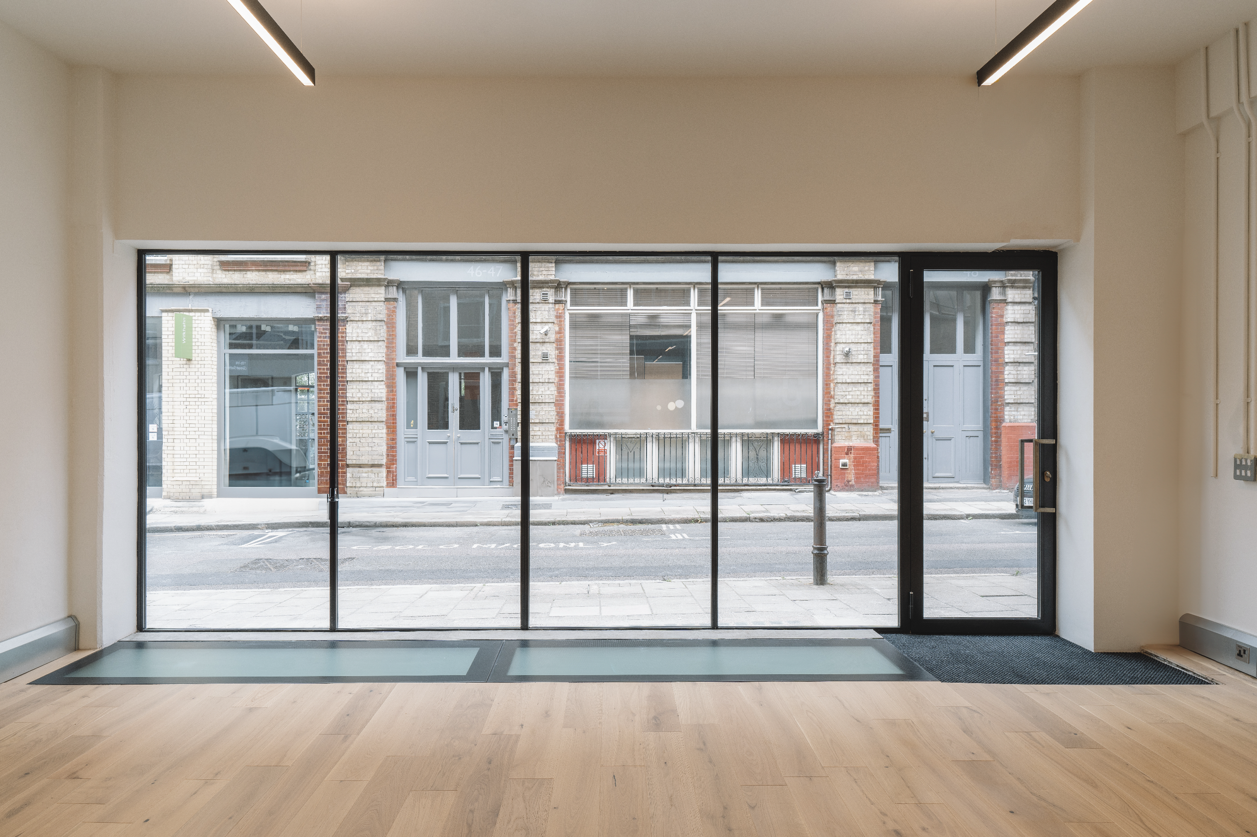 Empty room with wooden floor and a large glass storefront window and door looking out onto a city street with old brick buildings.