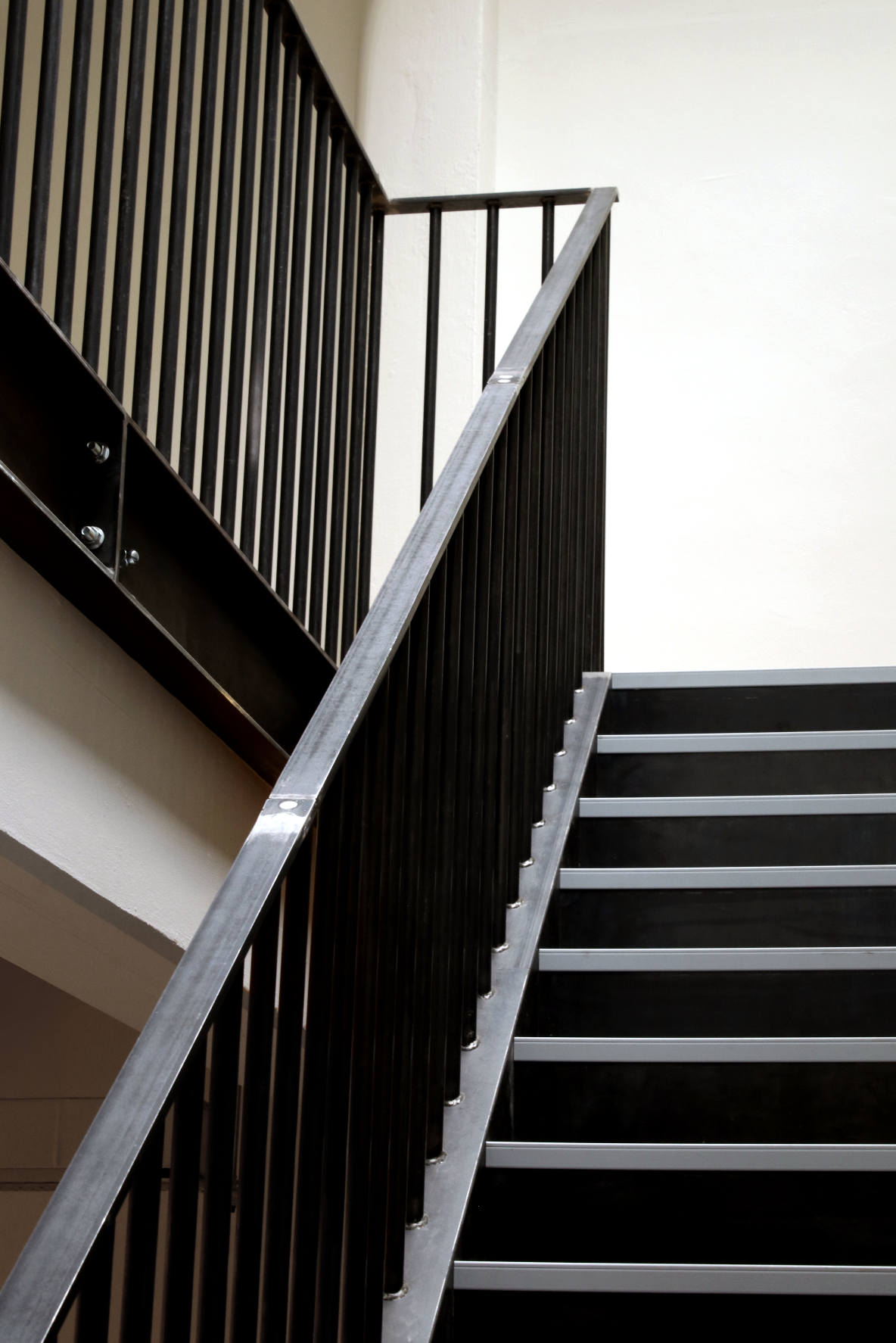 Close-up view of a modern staircase with black railings, white steps, and a metal handrail, against a white wall.