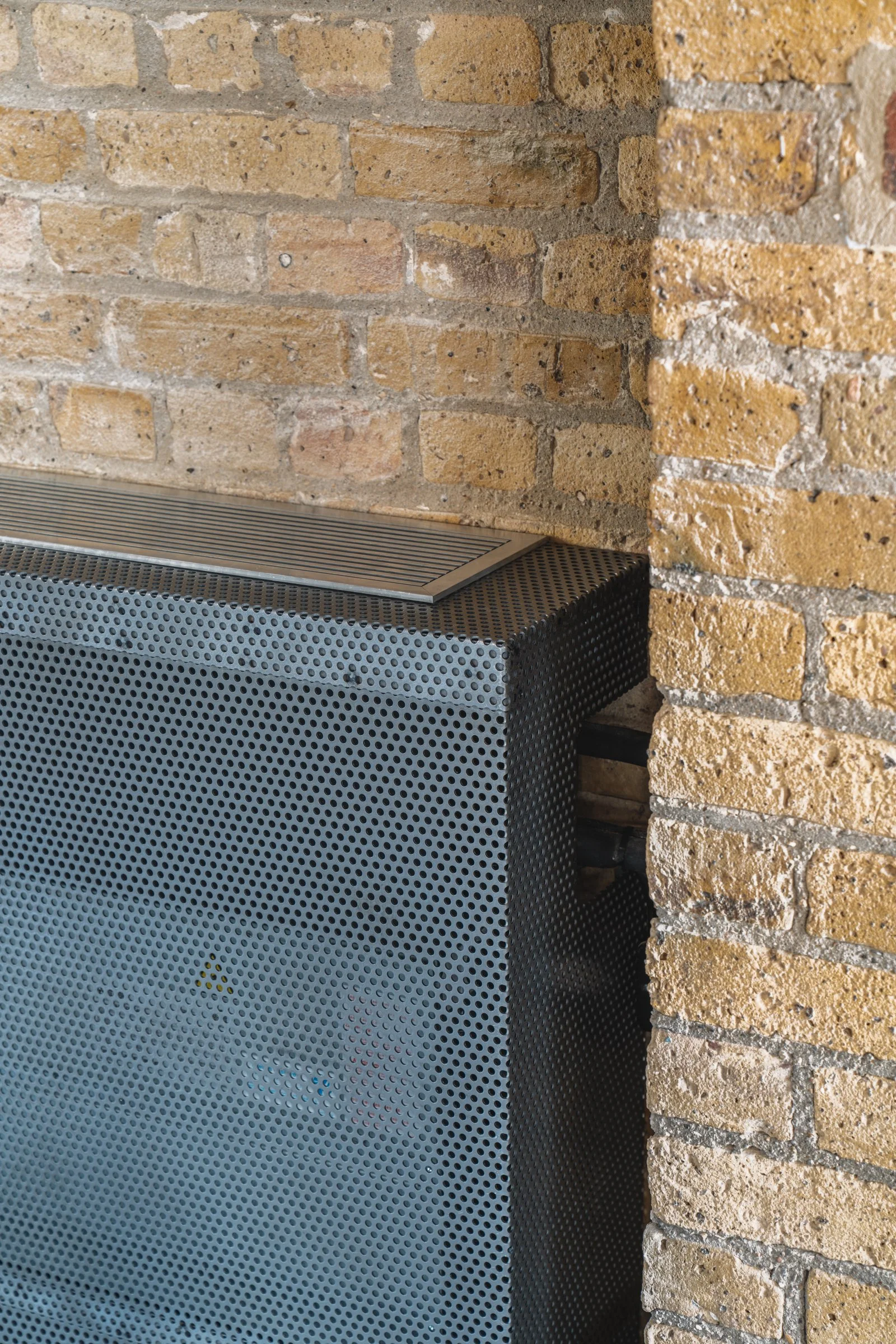 Close-up of a speaker with a perforated metal cover, positioned against a brick wall.