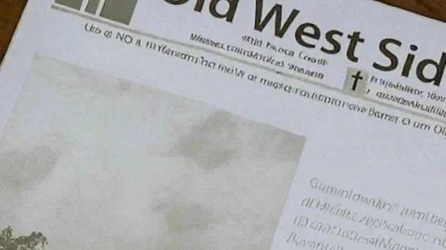 Close-up of a newspaper titled 'West Side' with some text and a section of an image visible.
