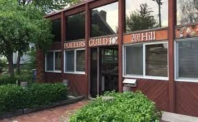 Exterior view of a building with a sign reading 'Potters Guild' and the address '201 Hill', surrounded by greenery.
