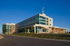 Modern multi-story building with large glass windows, a wind turbine on the roof, and a clear blue sky in the background.