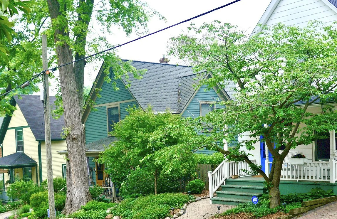 Residential neighborhood with colorful houses, lush green trees, and well-maintained garden and porches.