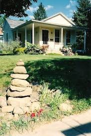 Front view of a house with a porch, surrounded by greenery, and a stone garden decoration in the front yard.