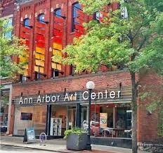 Exterior of the Ann Arbor Art Center building with a brick facade, large windows, and a colorful artistic installation on the upper part, surrounded by trees.