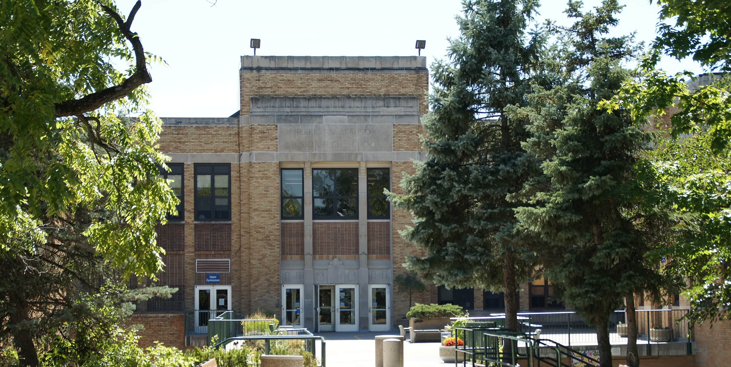 Exterior of a brick school building with trees and a small landscaped area in front.