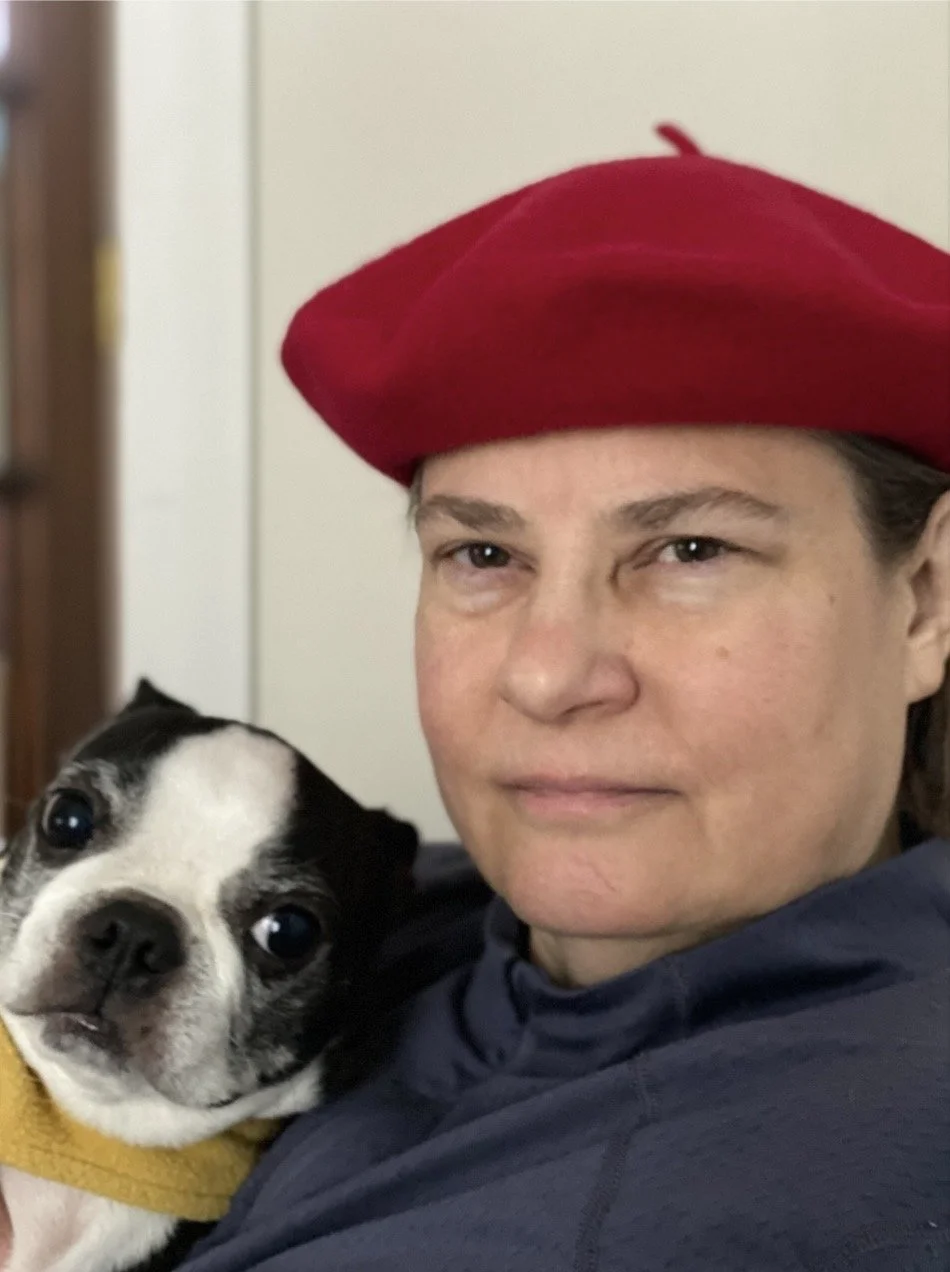 A person wearing a red beret holds a black and white puppy close to their face.