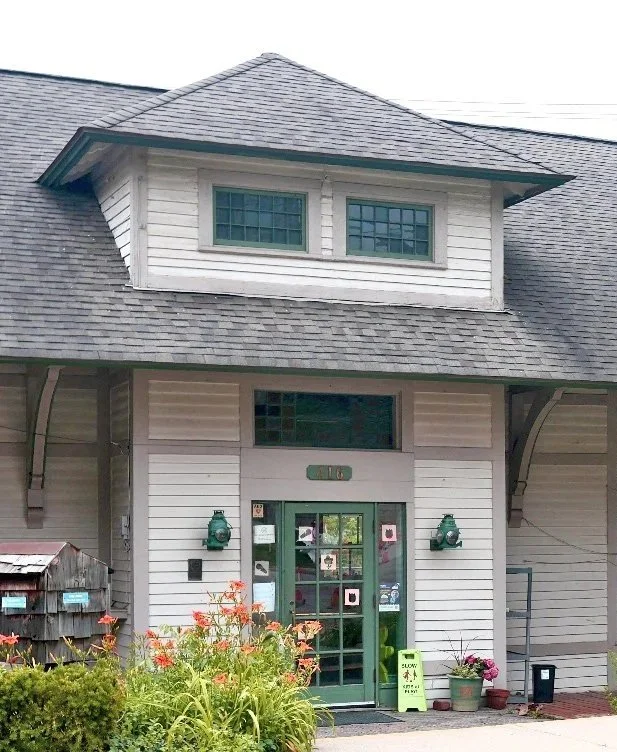 Exterior of a white house with two-story design, green front door decorated with pink and white paper flowers, flowerpots, and a small garden in front.