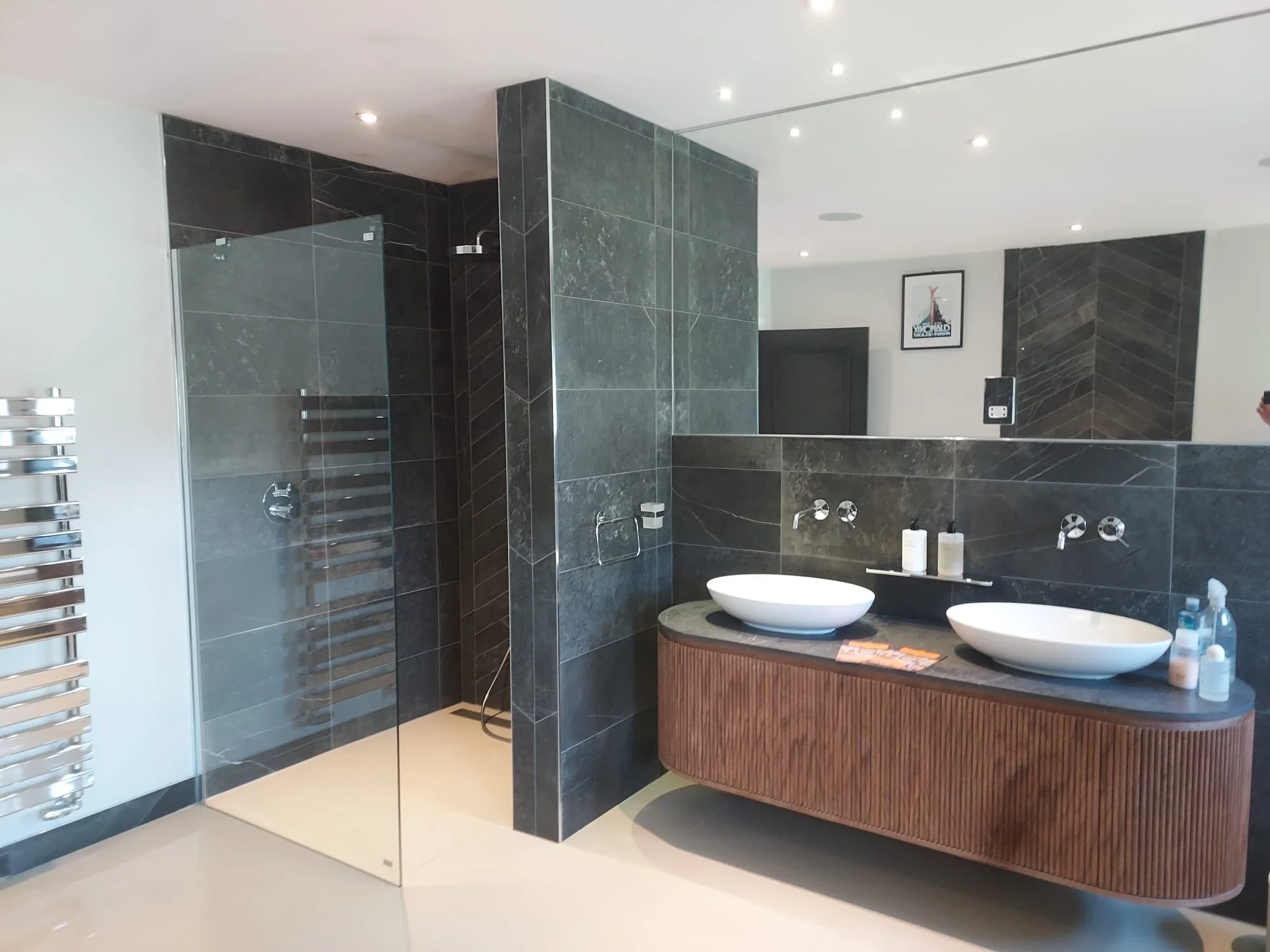 Modern bathroom with a dual-sink vanity, white vessel sinks, and a walk-in shower with glass doors and dark gray tile walls.