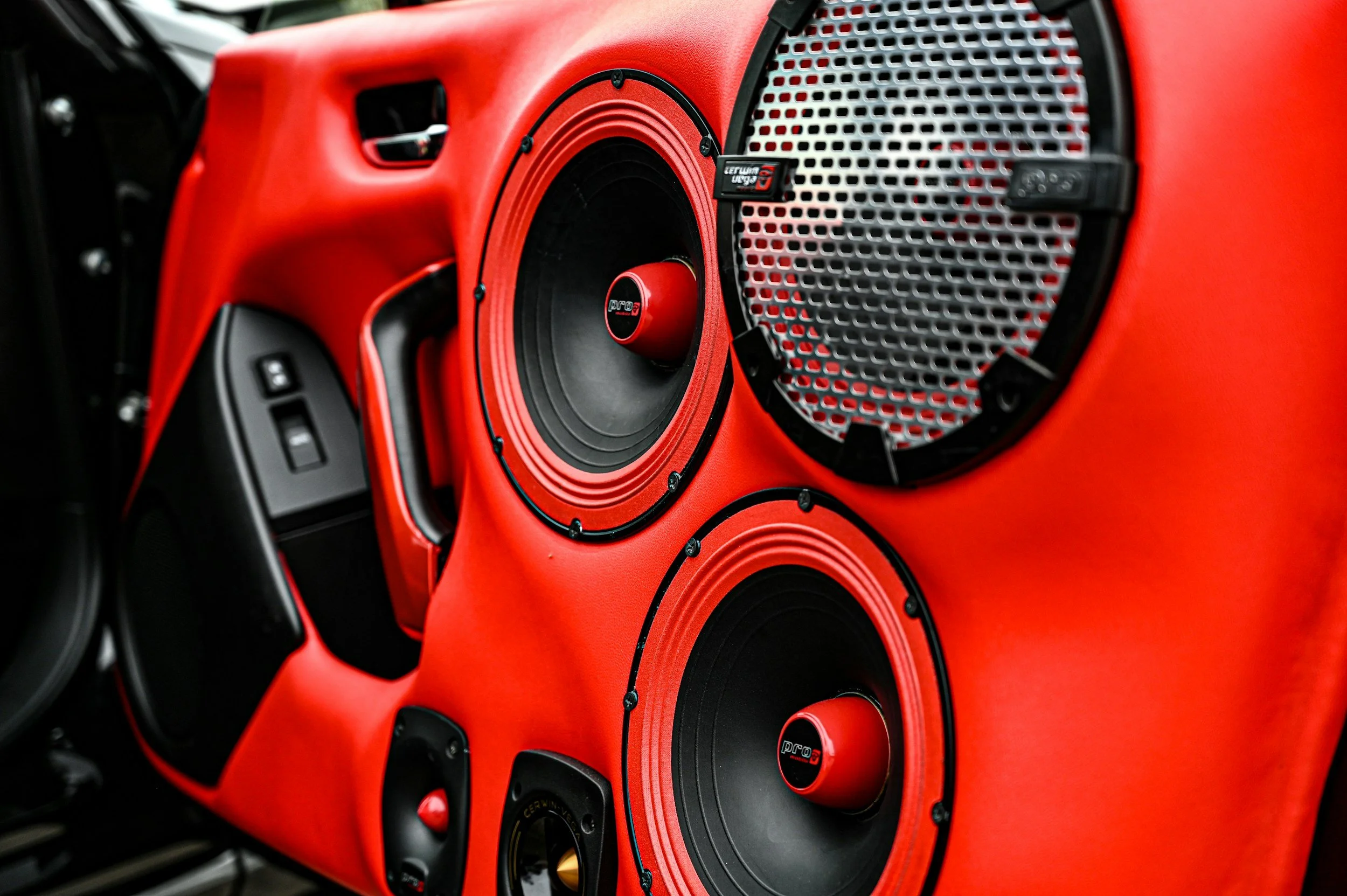 Red car interior with multiple large black and red speakers, including a TerraMomo speaker, mounted on the dashboard.