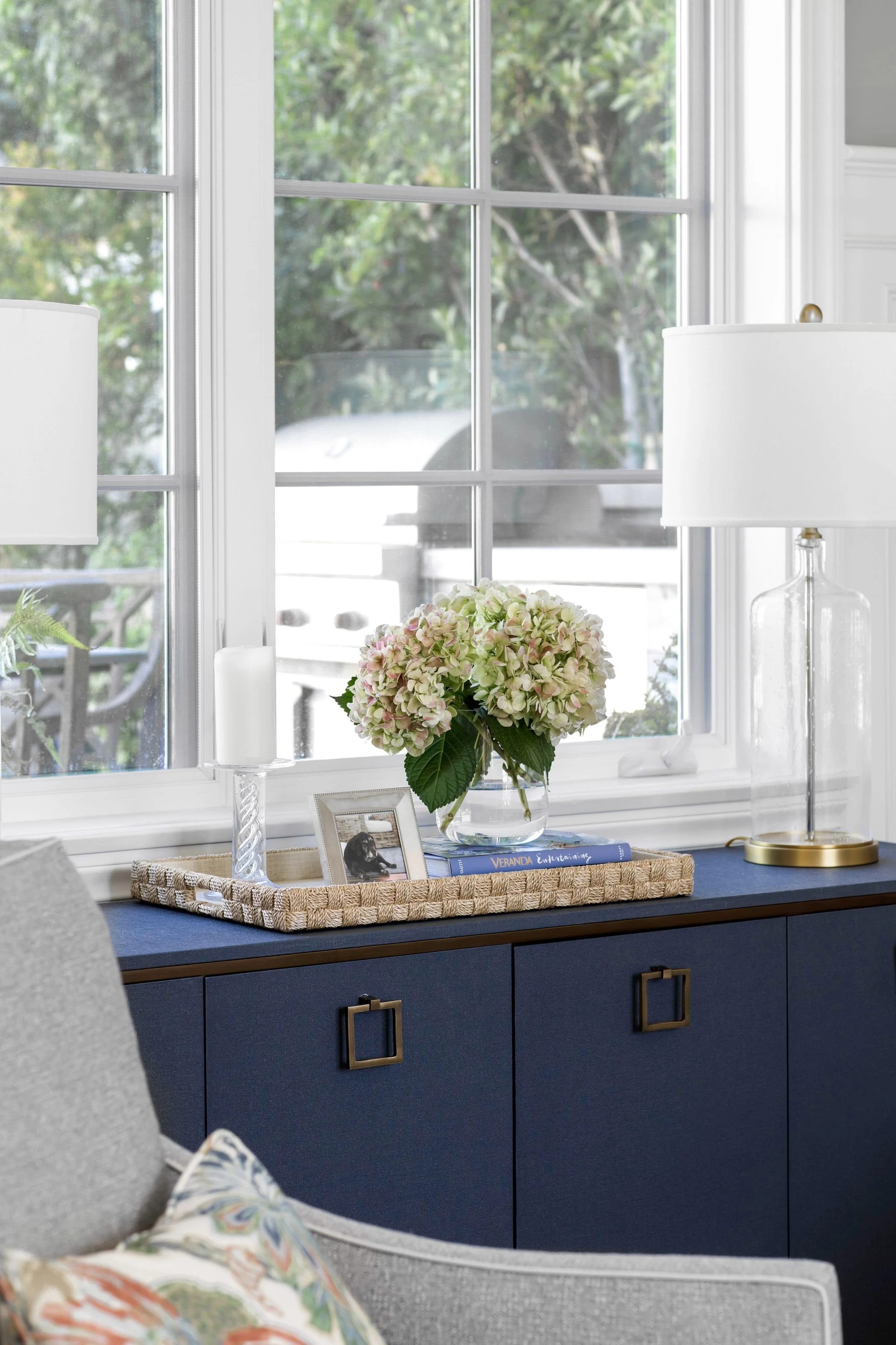 Blue sideboard styled with hydrangeas, books, and brass accents in a Pacific Palisades living room designed by Julie Beuerlein